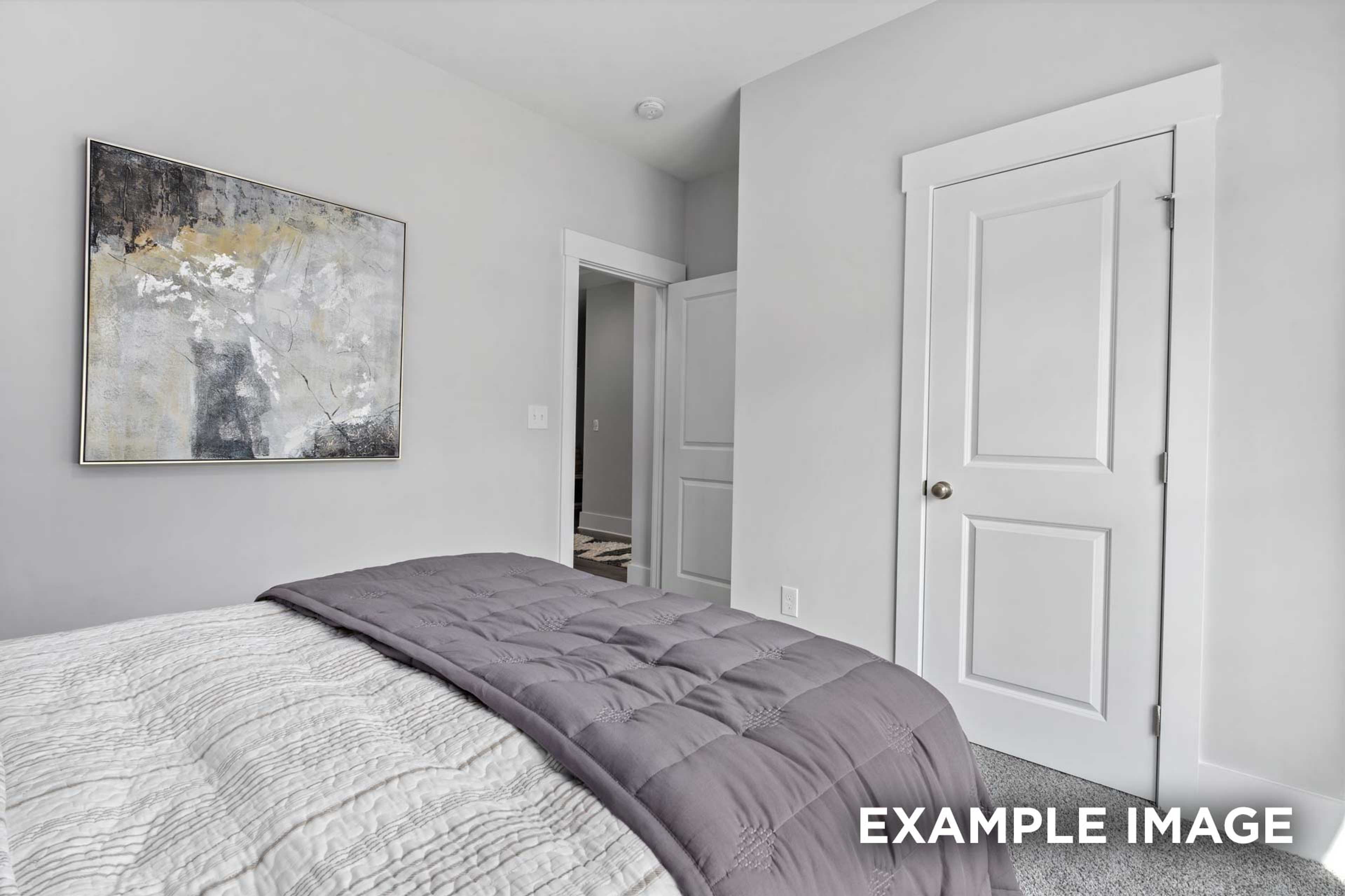 Master bedroom in The Franklin C Davidson Homes plan featuring gray walls, abstract wall art, white doors, and plush bed