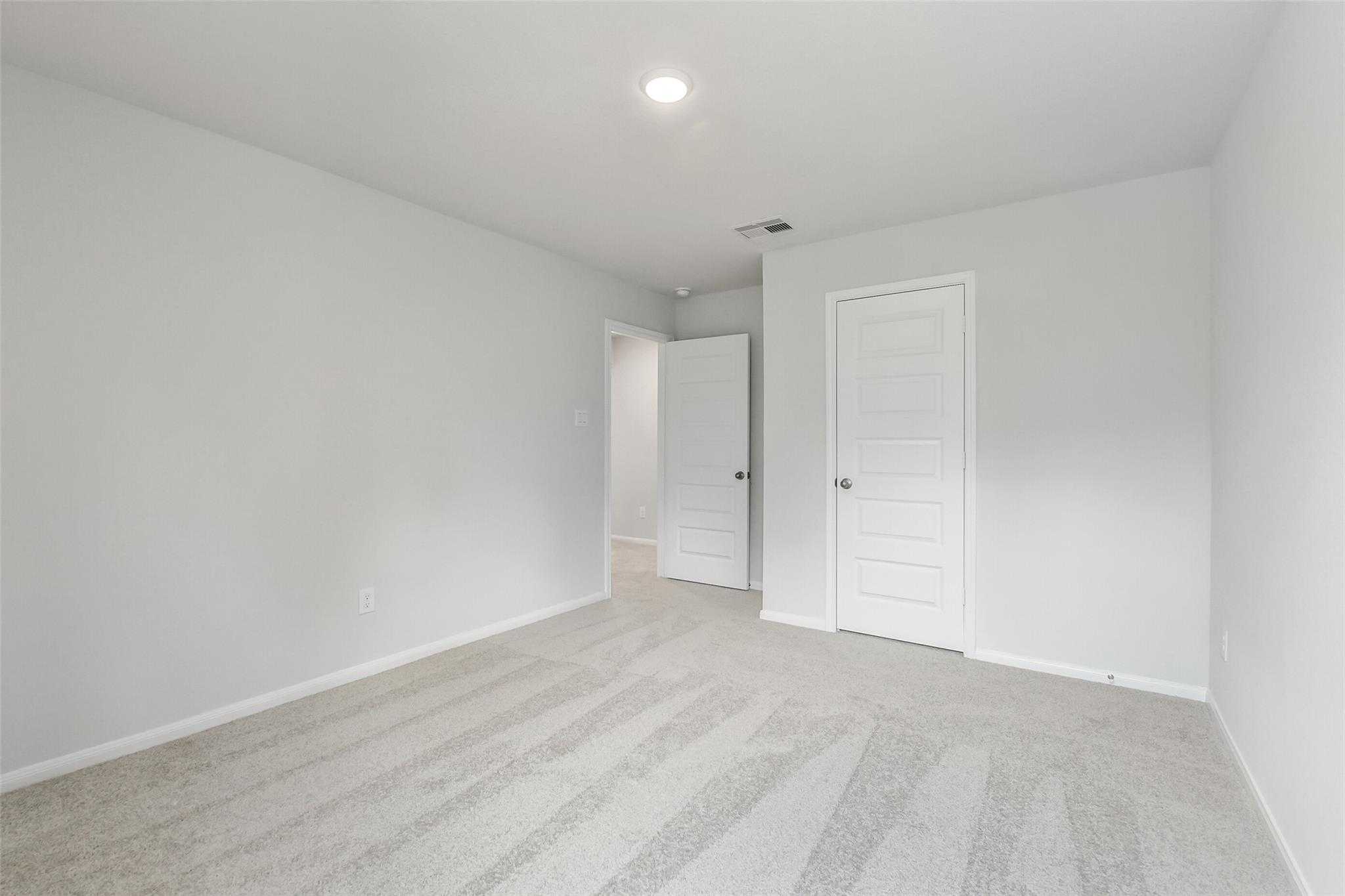 Bright secondary bedroom with gray walls, white double doors, recessed lighting, and plush carpet in Davidson Homes The Sabine E, Conroe TX