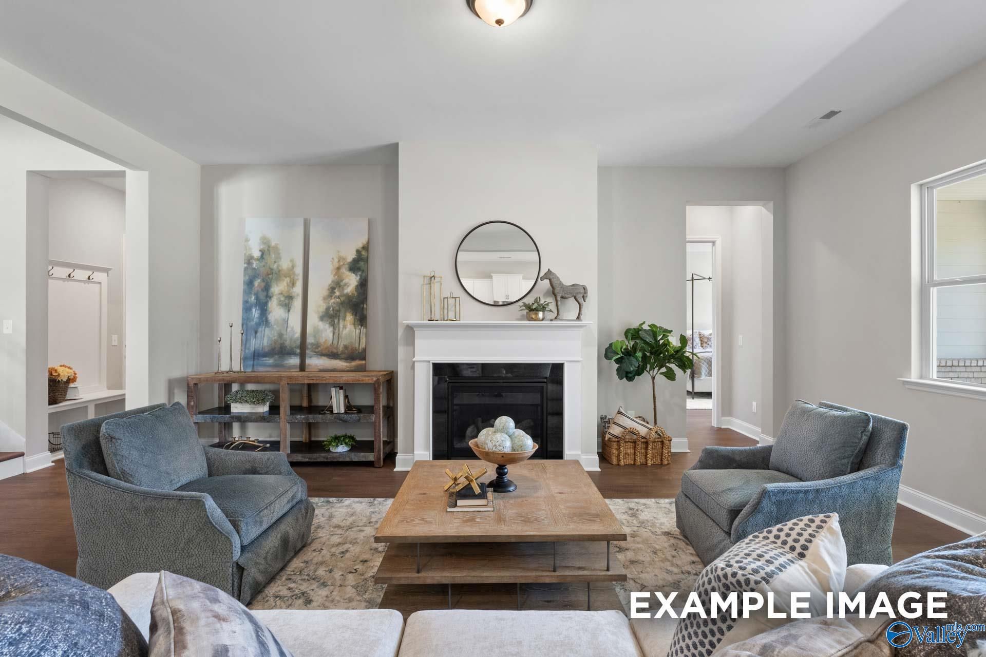 Cozy living room with white fireplace, blue velvet armchairs, and wooden coffee table in Evermore Homes The Haven E, Owens Cross Roads, Alabama