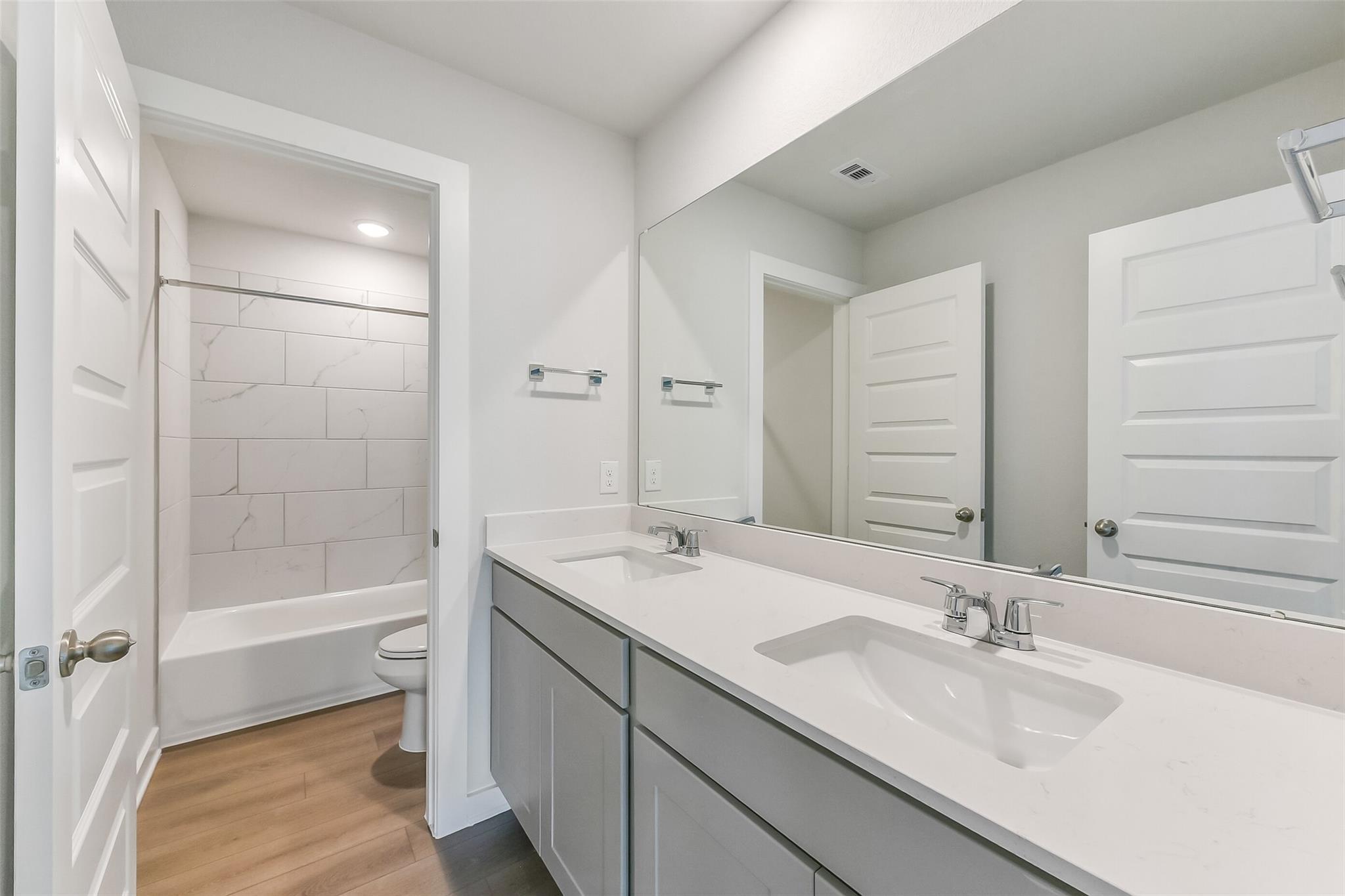 Modern bathroom with double vanity, white quartz counters, soaking tub and subway tile in Davidson Homes The Tierra C, Dayton, Texas