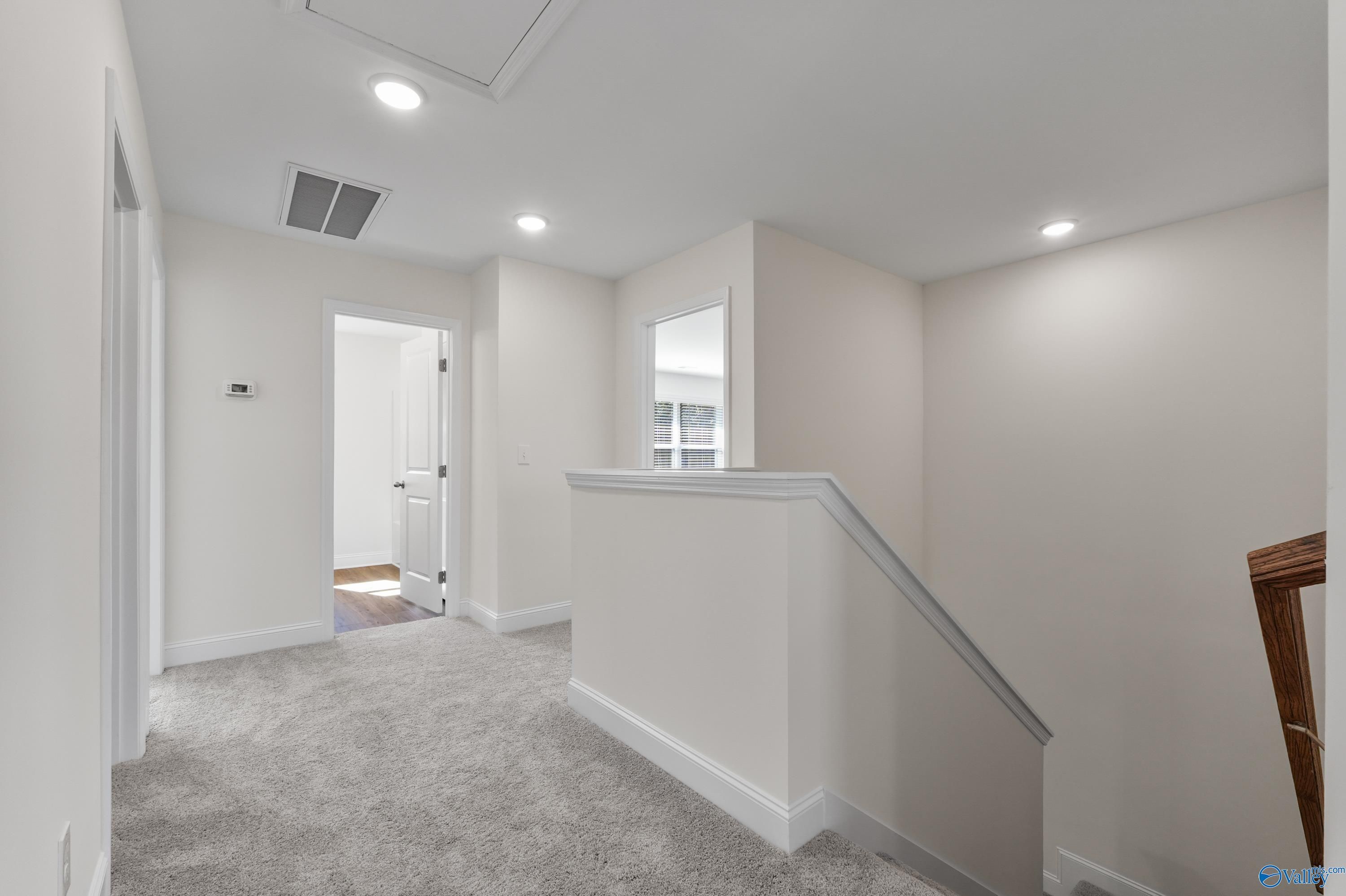 Bright upstairs hallway with beige carpet, white walls, wooden railing, and open staircase in Davidson Homes The Shelby A, Athens, Alabama