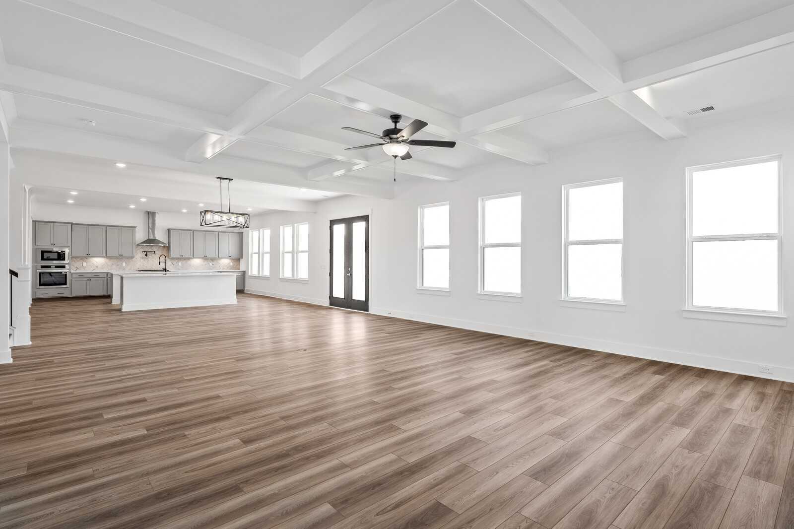 Spacious open-concept kitchen-living area with coffered ceiling, hardwood floors, gray cabinets, white island, and large windows in The Alston A home, Murfreesboro