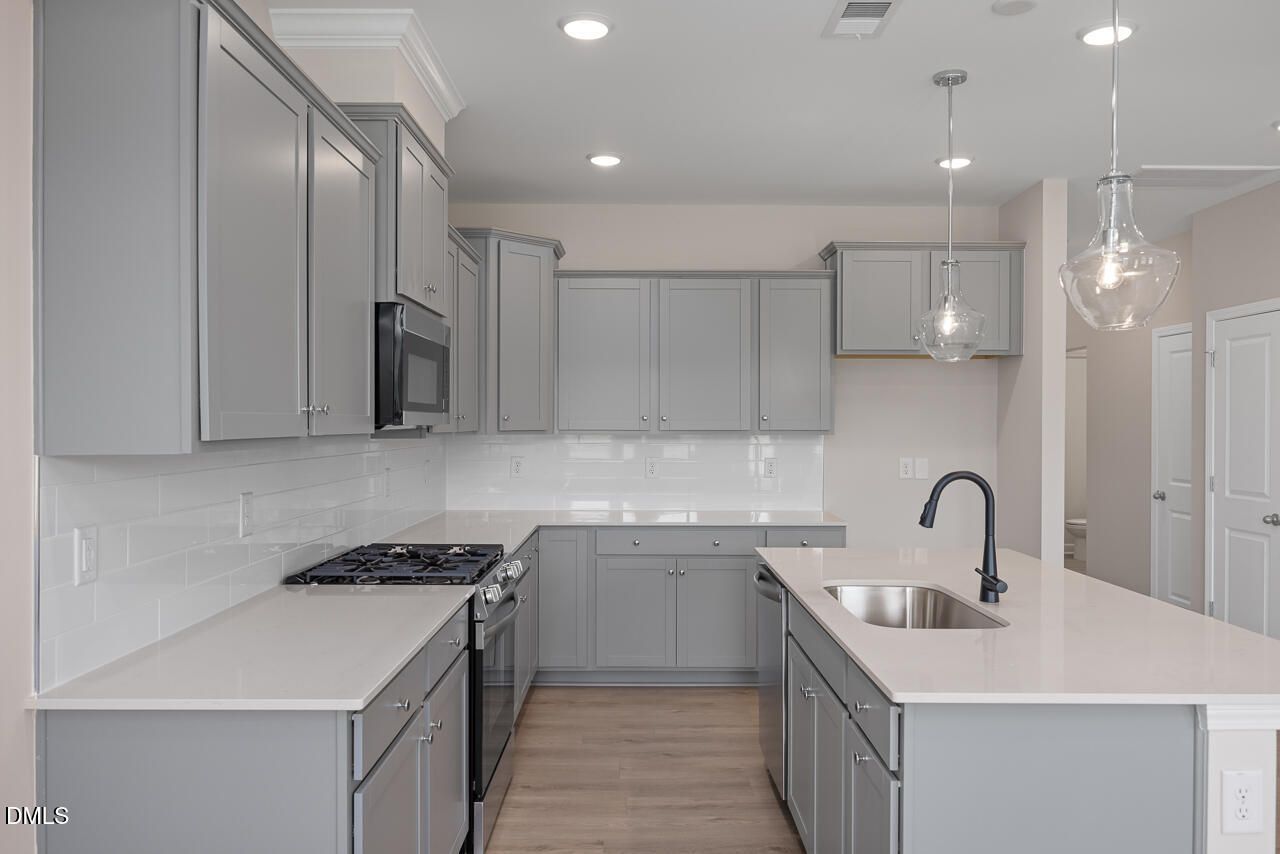 Modern kitchen with gray cabinets, quartz countertops, and island in The Graham floor plan at Springvale, Fuquay-Varina.