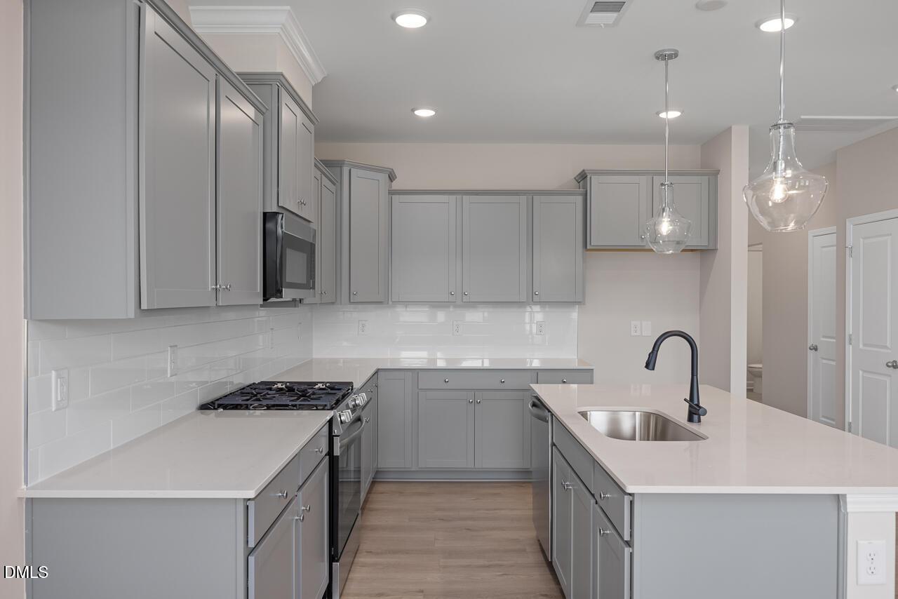 Modern kitchen with gray cabinets, quartz countertops, and island in The Graham floor plan at Springvale, Fuquay-Varina, NC.
