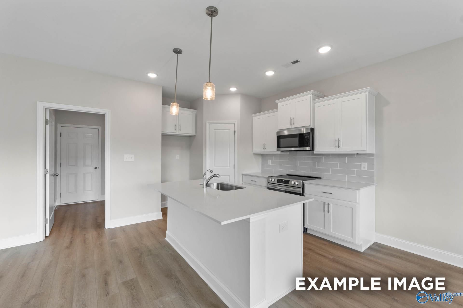 Modern white kitchen with shaker cabinets, large island sink, stainless microwave and oven in Davidson Homes The Butler, Owens Cross Roads