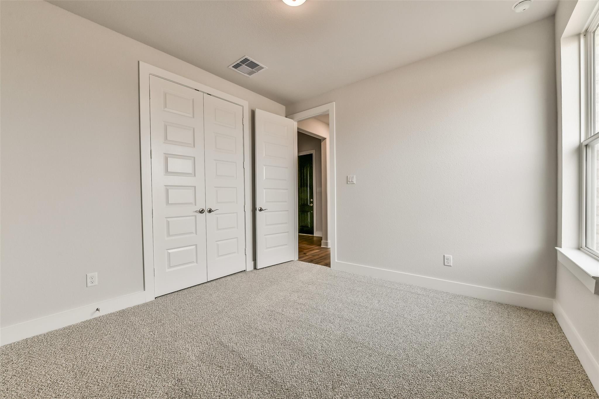 Spacious secondary bedroom with neutral walls, beige carpet, double closet doors, and window in Davidson Homes The George A, Lago Mar