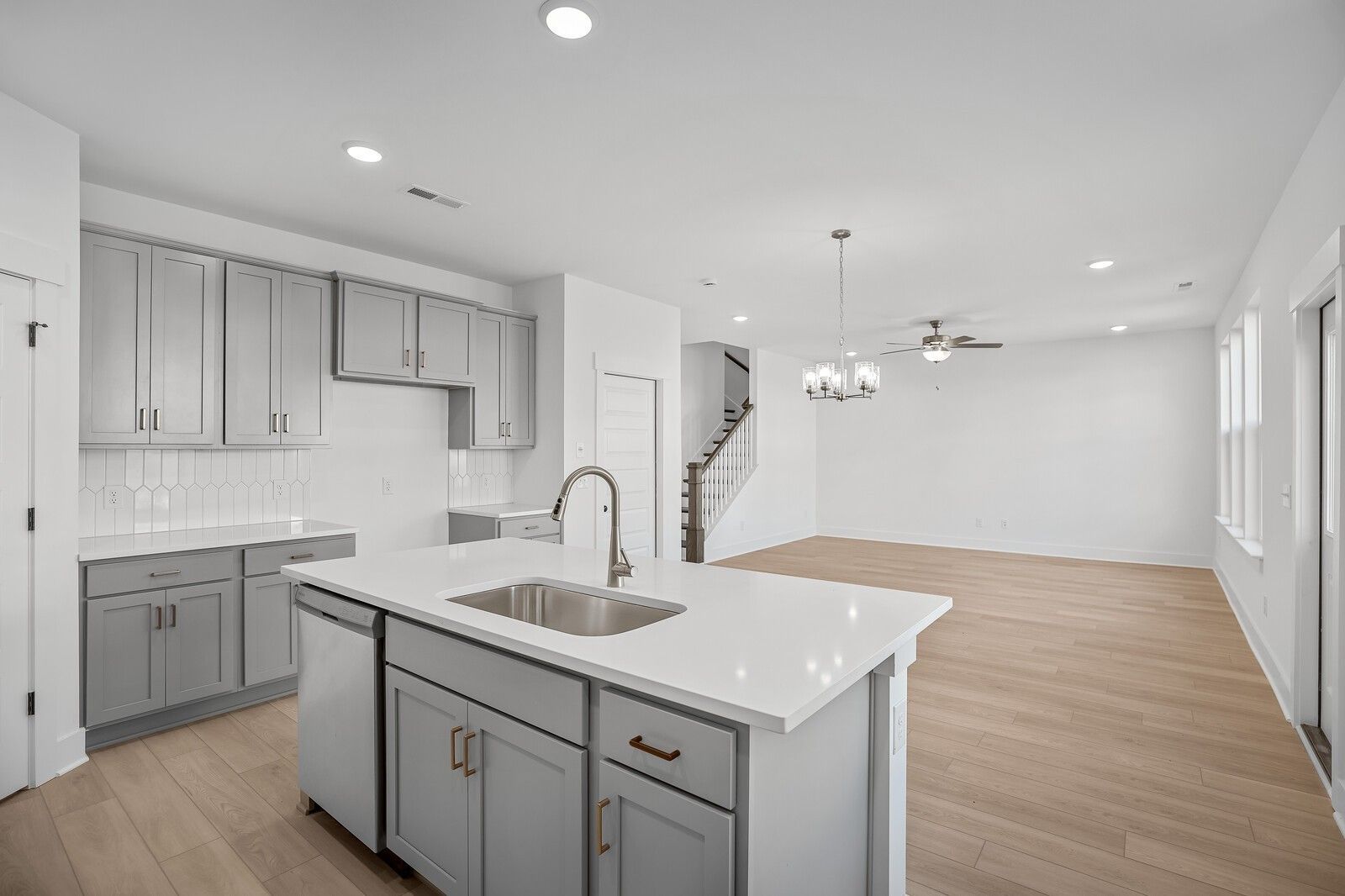Modern open-concept kitchen with gray shaker cabinets, white quartz island, stainless sink, hardwood floors in The Logan C, Gallatin, TN