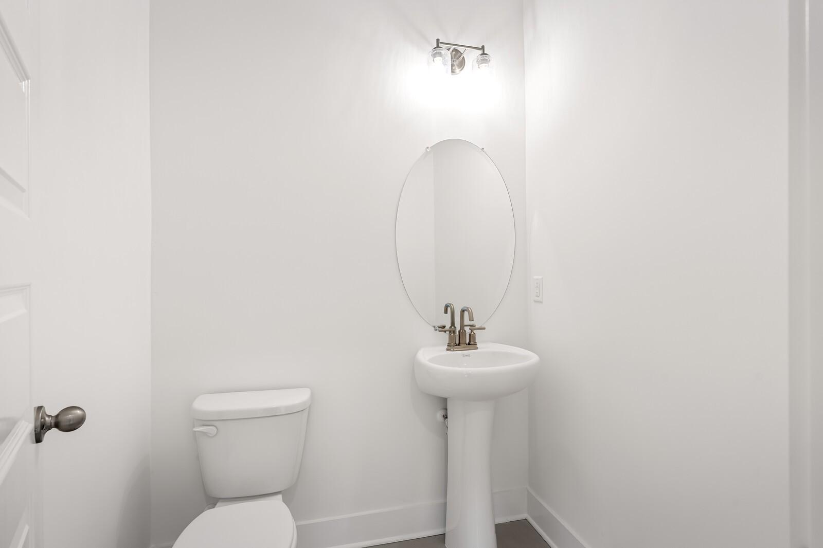 Bright white powder room with pedestal sink, round mirror, and sconce lighting in Davidson Homes The Ash C, Mt. Juliet, Tennessee
