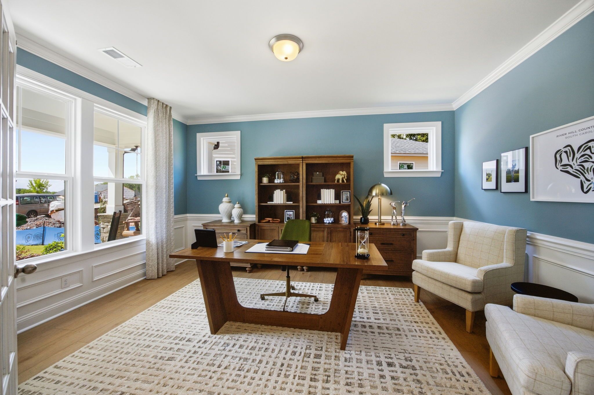 Spacious home office at Enclave at Belmont in Belmont NC with wooden desk, blue walls, bookshelves, and large windows