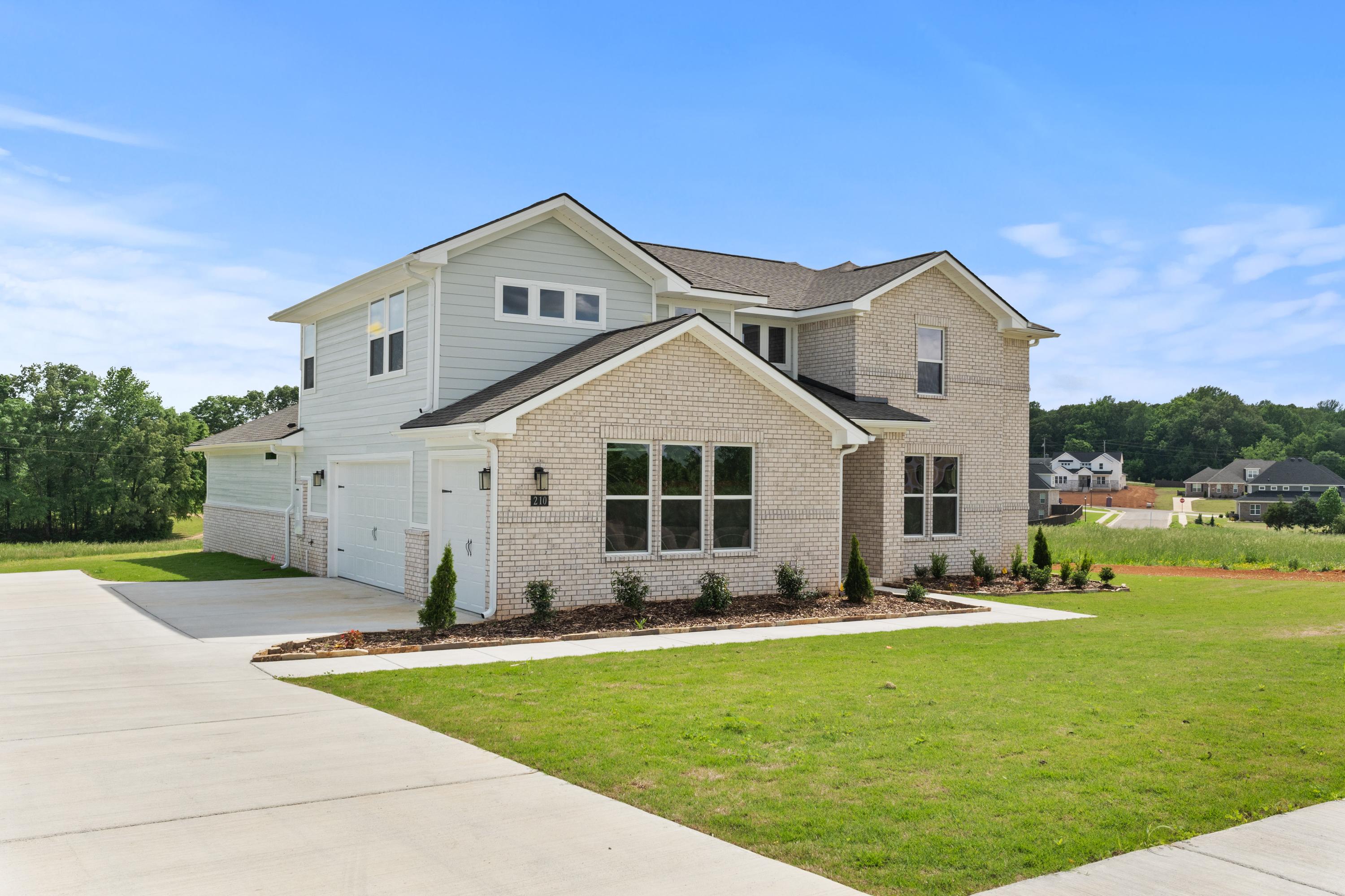 Modern exterior of The Haven E single-family home with light gray siding, brick accents, 3-car garage, and landscaped yard