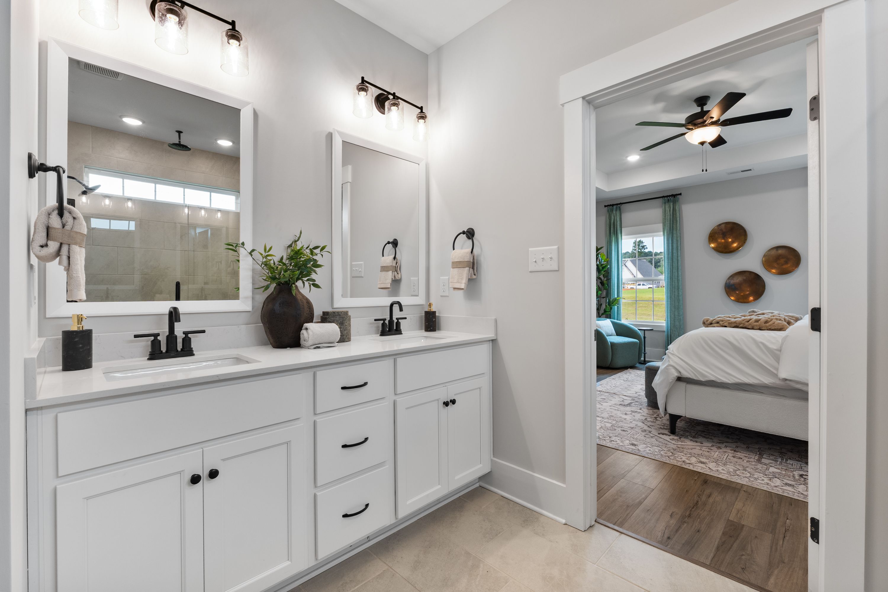 Spacious primary bathroom at River Road Estates in Decatur Alabama with double white vanity, mirrors, plants and open bedroom view