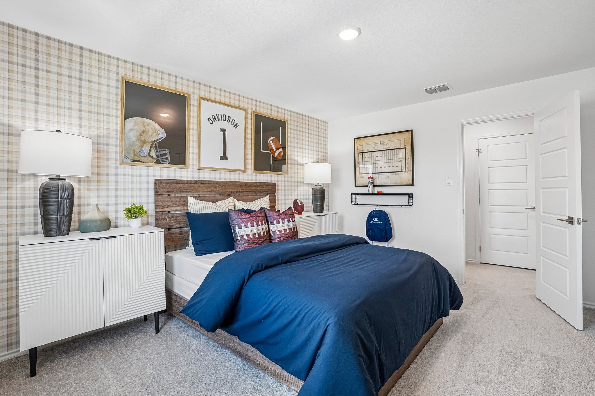 Football-themed bedroom at Morgan Meadows in San Antonio by Davidson Homes with plaid wallpaper and modern wood furniture.