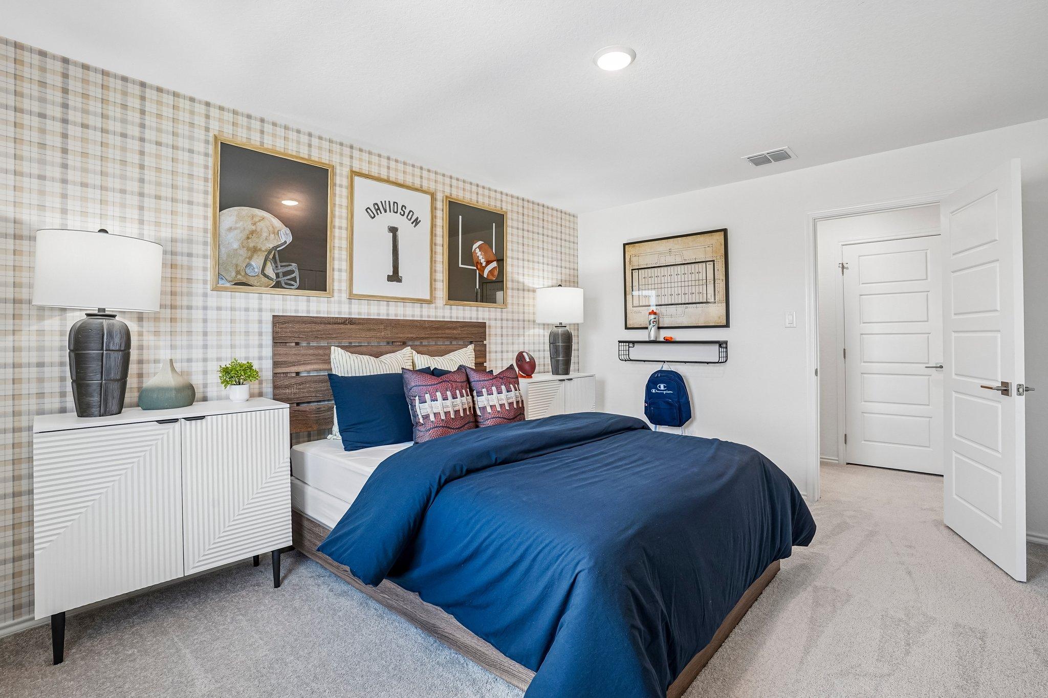 Football-themed bedroom at Morgan Meadows in San Antonio by Davidson Homes with plaid wallpaper and modern wood furniture.
