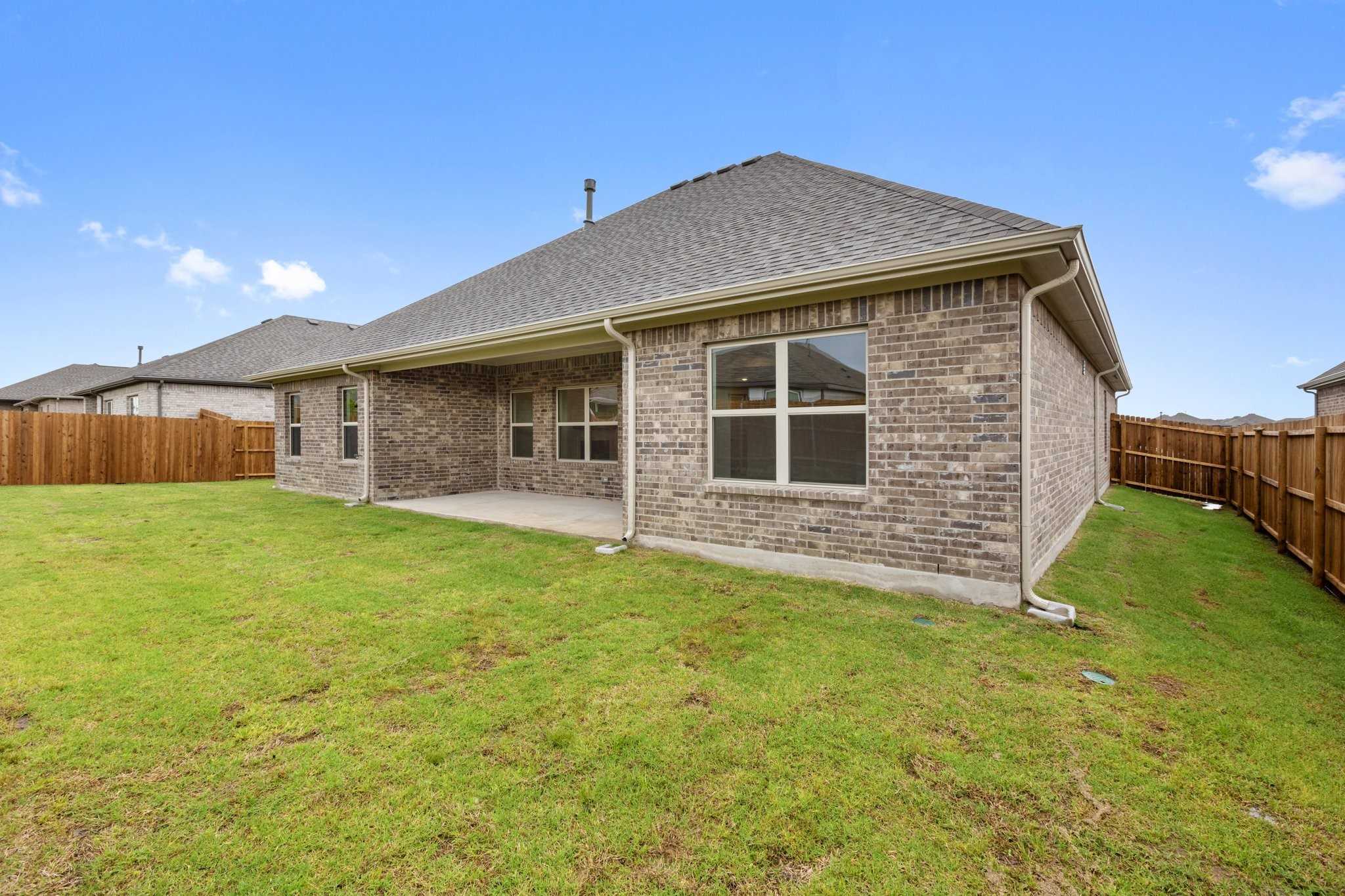 Brick side exterior of Davidson Homes Rockford C 4-bedroom with covered patio, green yard, wood fence in Waverly Estates, Josephine, Texas