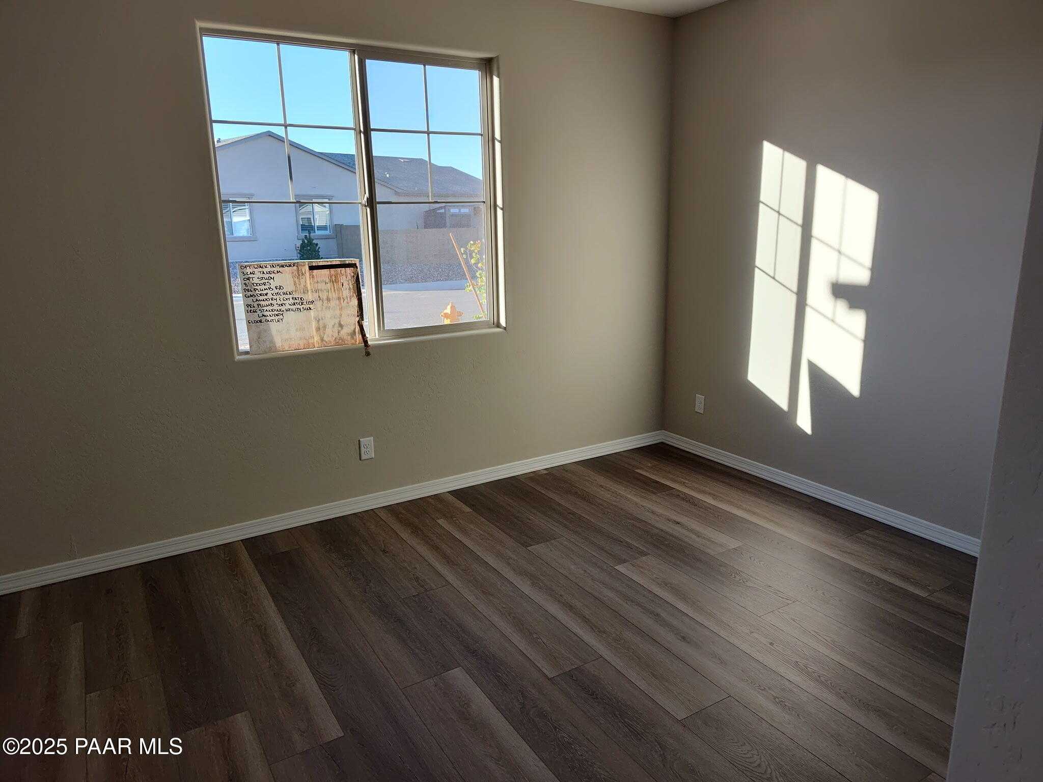 Sunlit empty bedroom with beige walls, luxury vinyl plank flooring, and large window in Davidson Homes Inspiration A, Prescott Valley, AZ