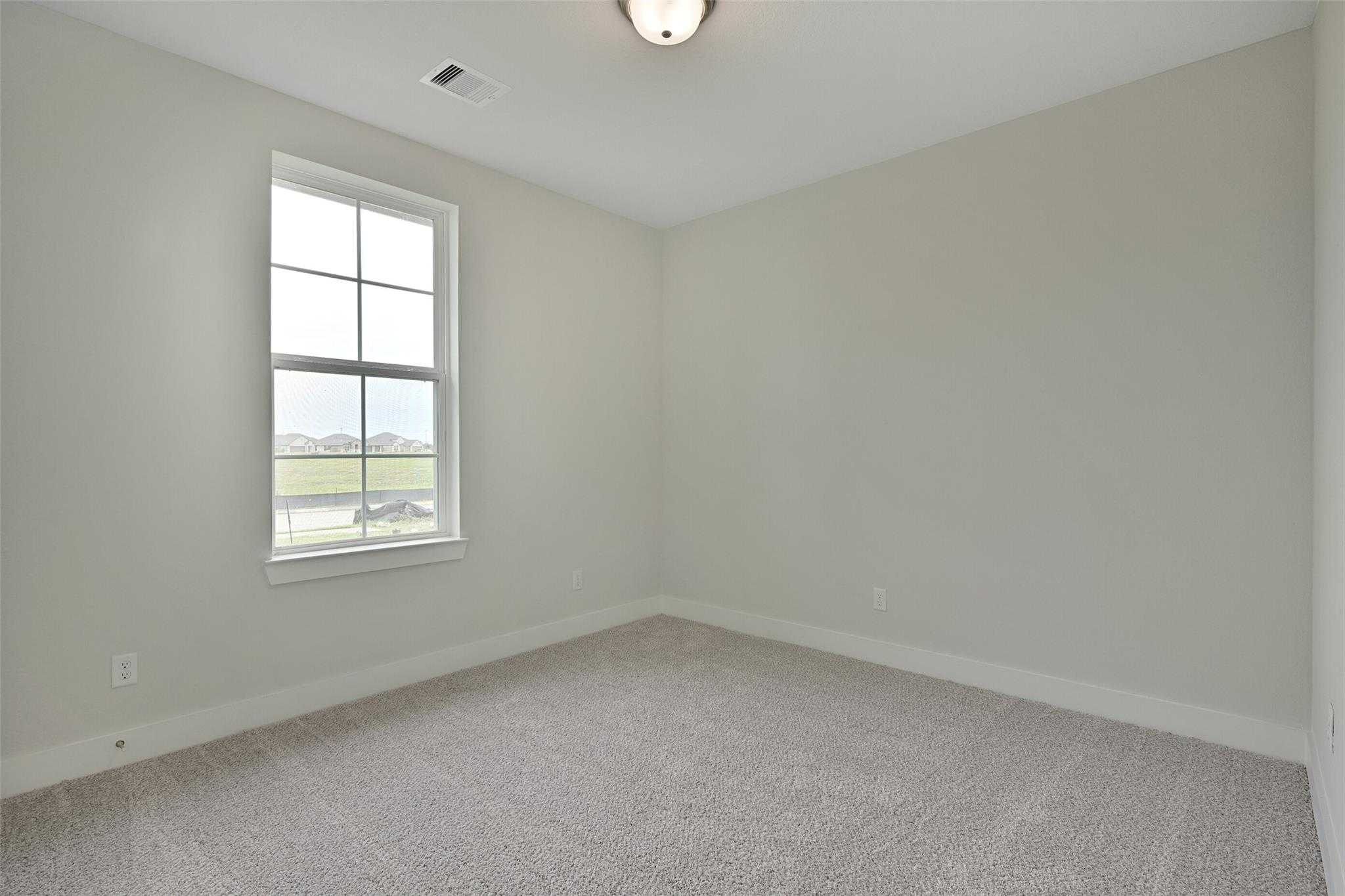 Bright secondary bedroom with neutral walls, carpet flooring, and scenic pond view window in Davidson Homes The Edward A, Lago Mar, Texas