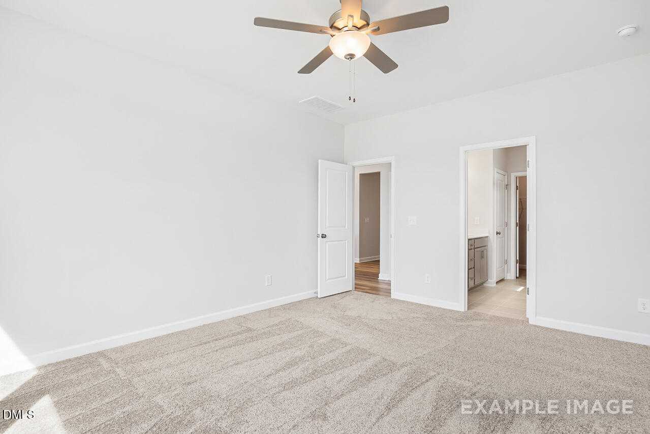Neutral bedroom with beige carpet, white walls, ceiling fan, and bathroom doorway in Davidson Homes The Daphne C, Lillington, NC