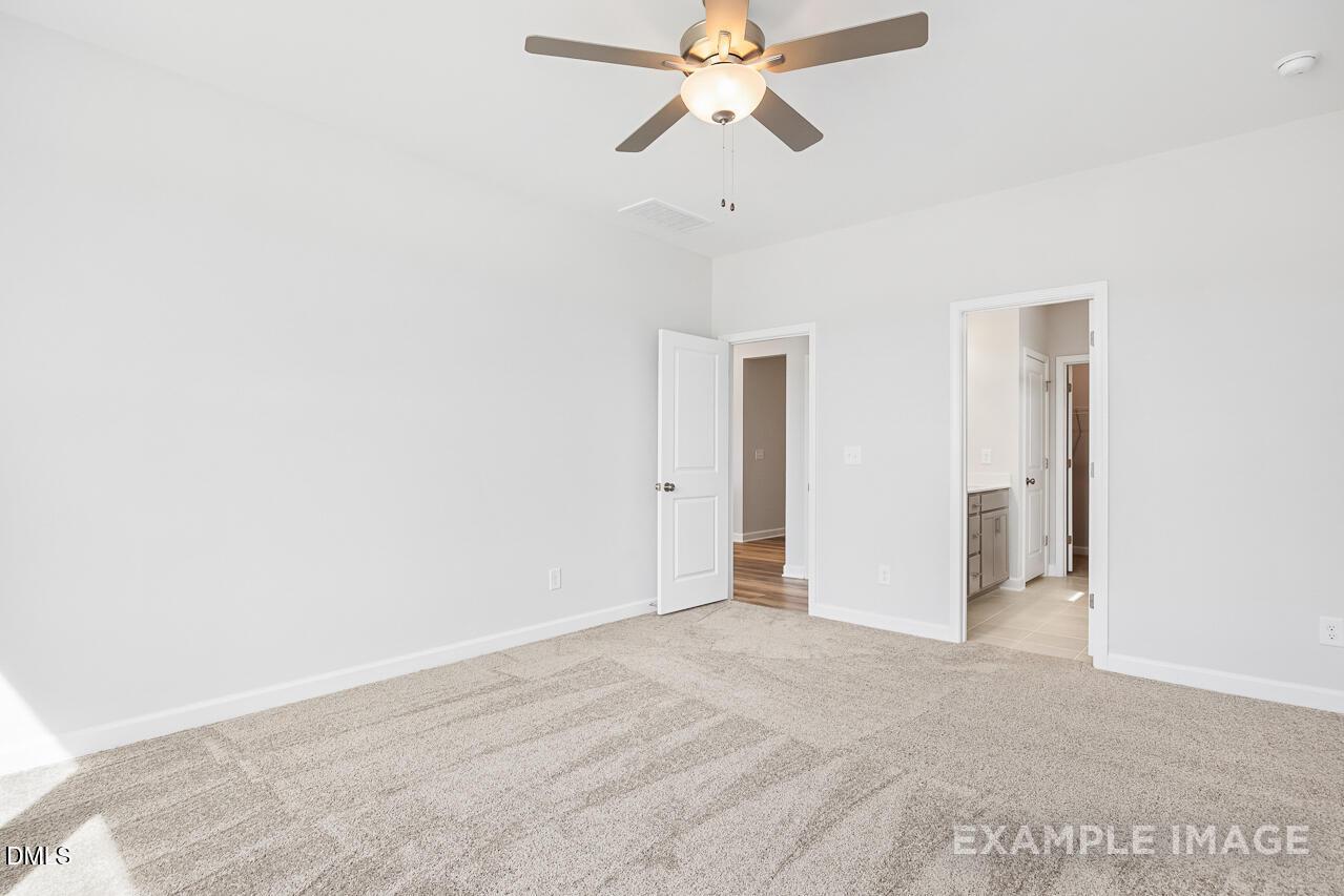 Bright bedroom with ceiling fan, beige carpet, and en-suite bathroom door in Davidson Homes The Daphne C, Zebulon, NC