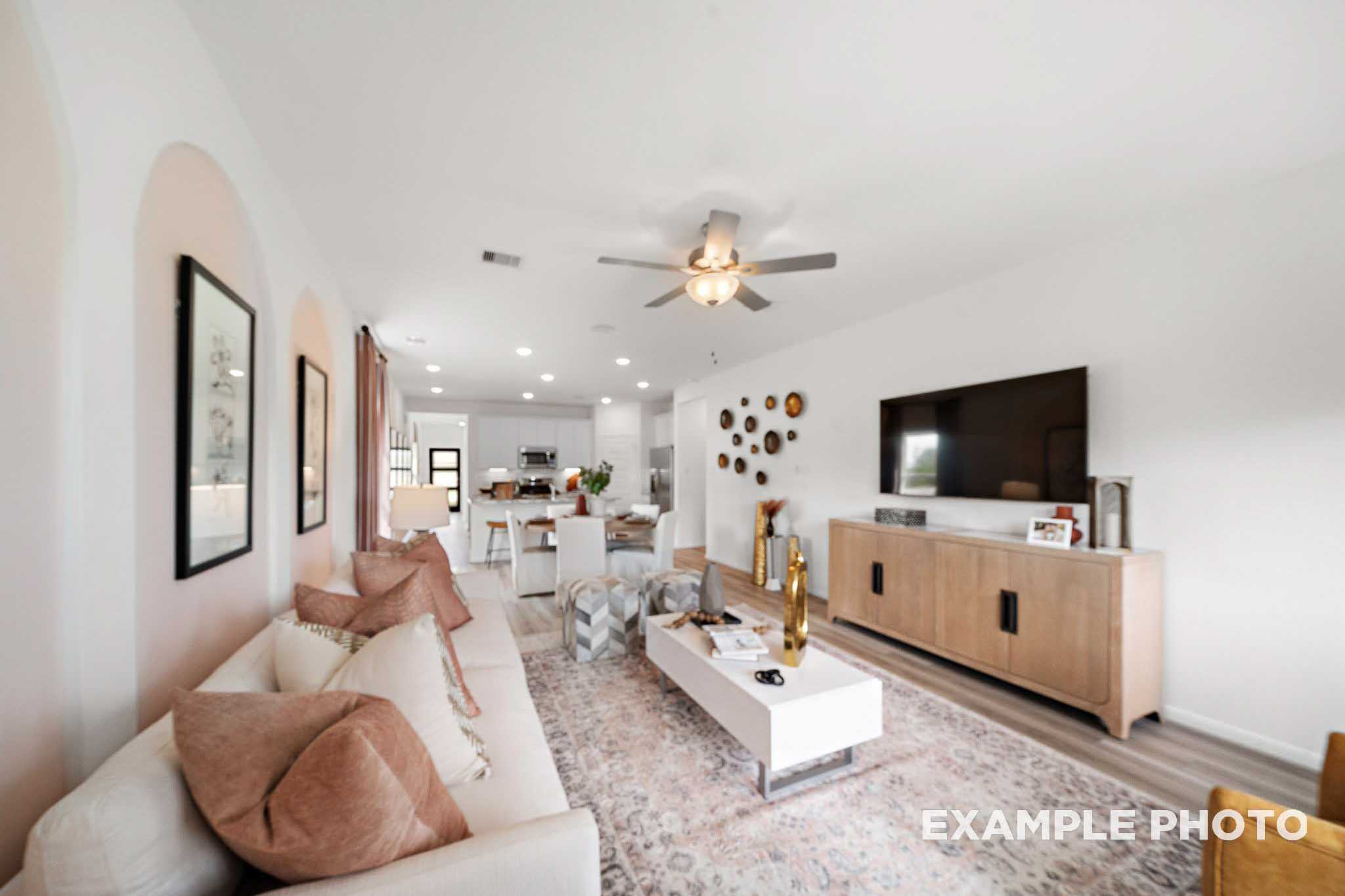 Open-concept living room in The Sabine E with white sofa, wooden credenza, TV, and adjacent modern kitchen