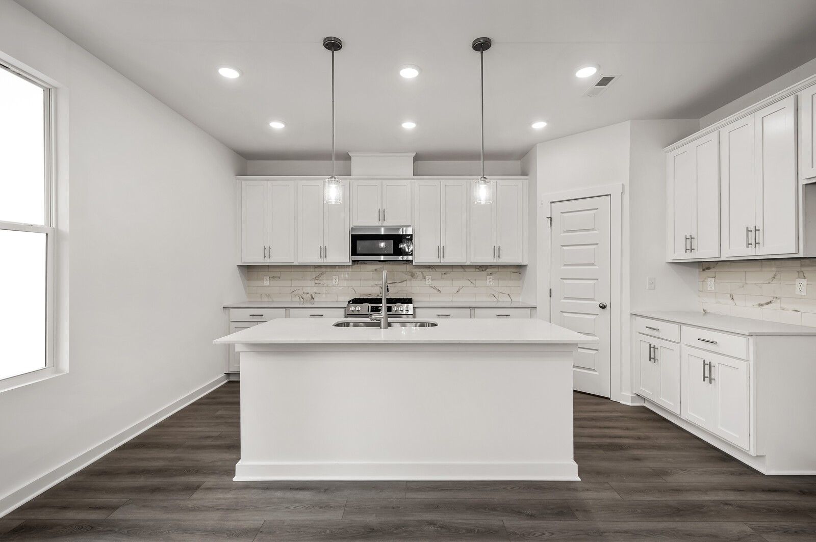 Modern white kitchen with island, pendant lighting, and stainless appliances in The Logan C floor plan at Calista Farms.