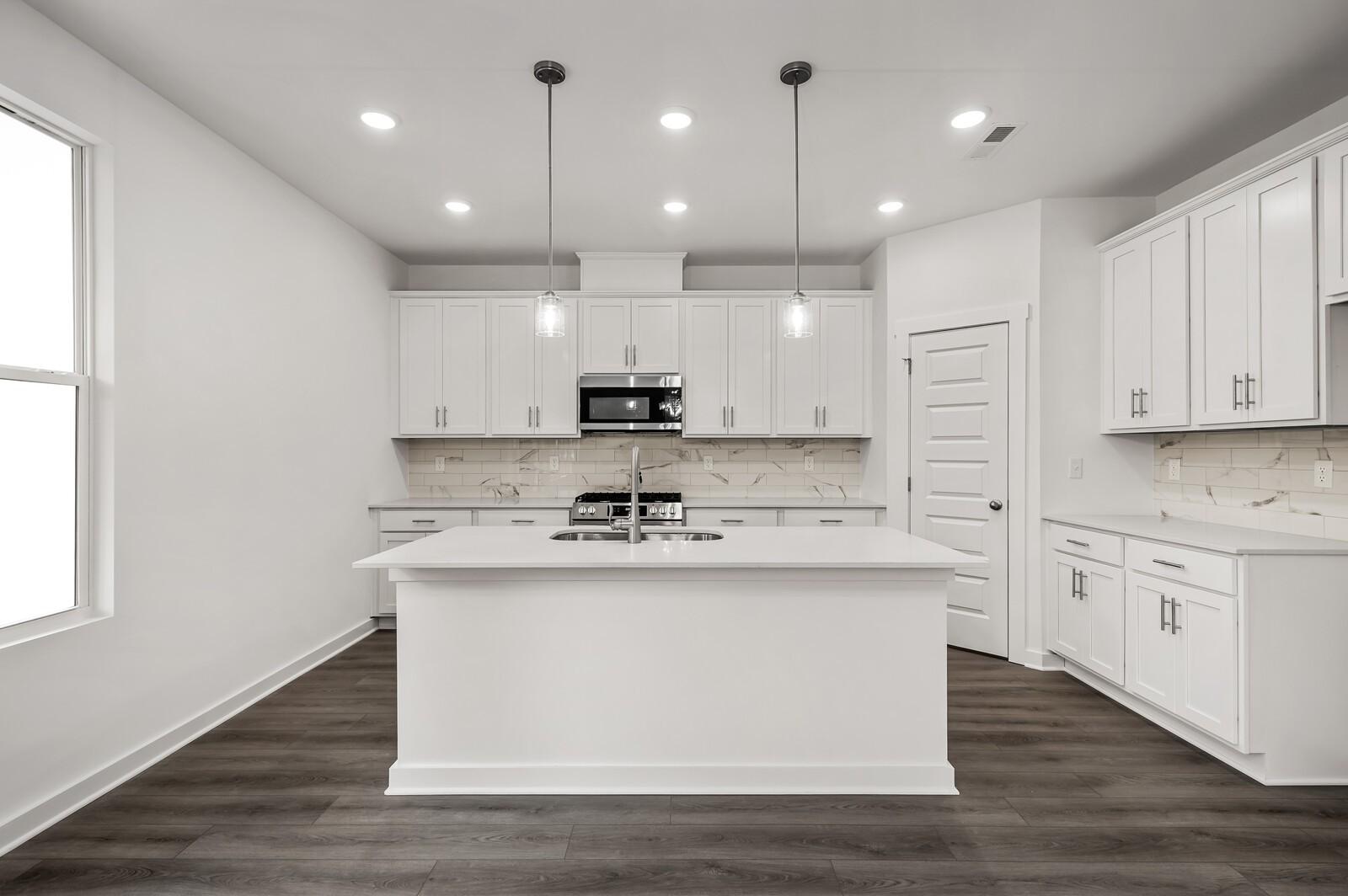 Modern white kitchen with island, pendant lighting, and stainless appliances in The Logan C floor plan at Calista Farms.