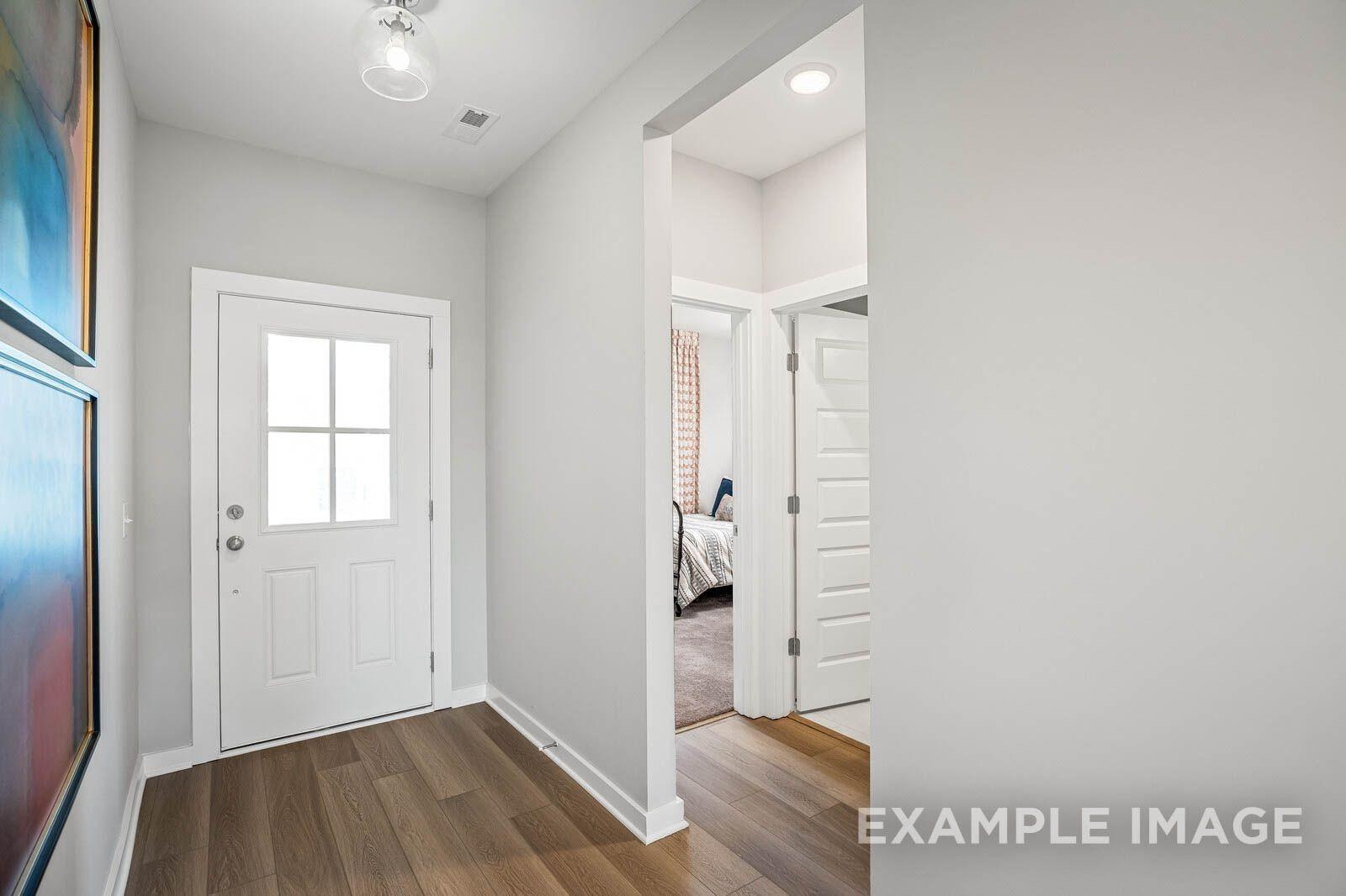 Bright entryway with white paneled door, light gray walls, hardwood floors, and bedroom view in Davidson Homes Franklin B, White House, TN