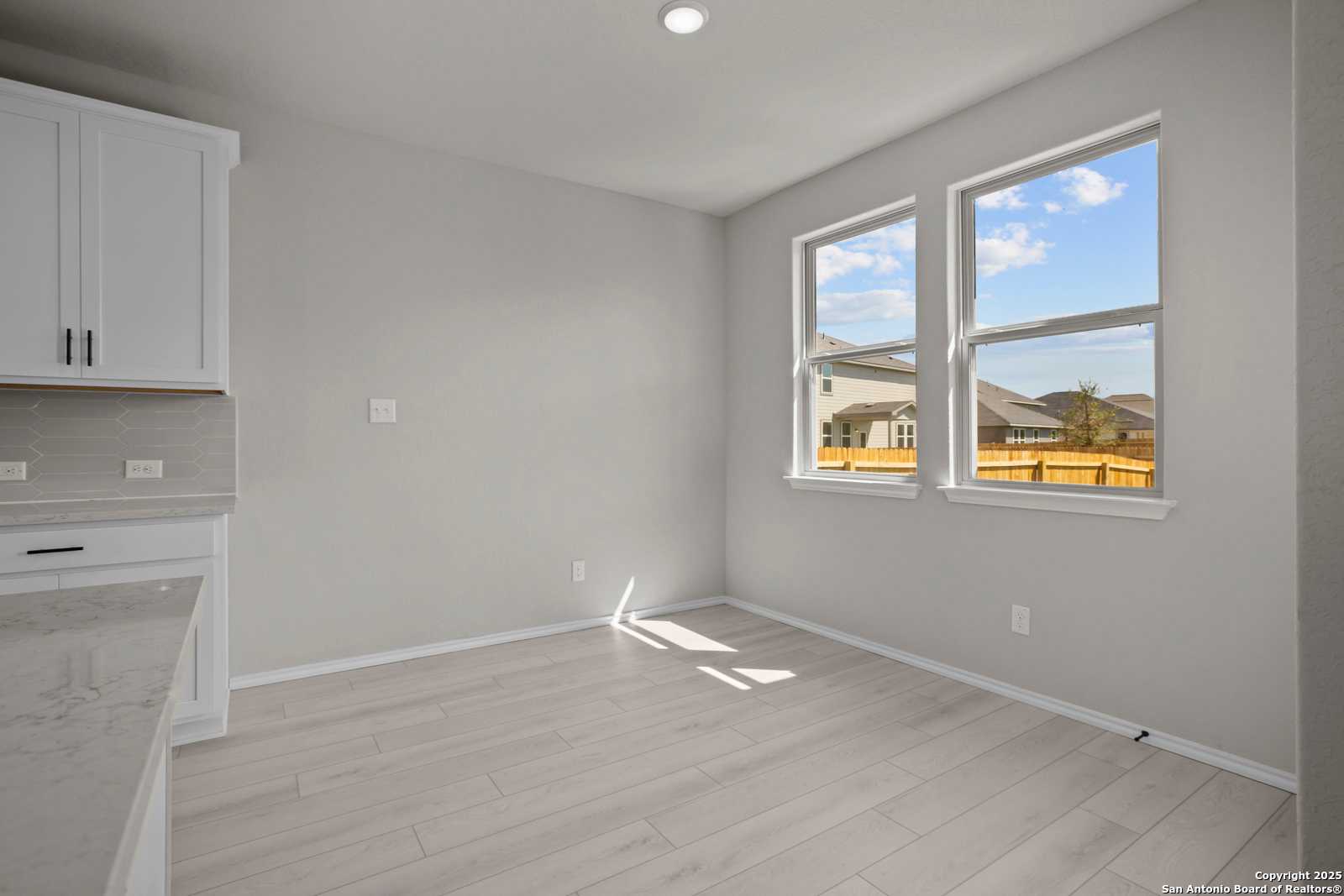 Bright kitchen nook with white cabinets, gray walls, luxury vinyl plank floors, and large sunny windows in Davidson Homes The Asheville E, Converse, Texas