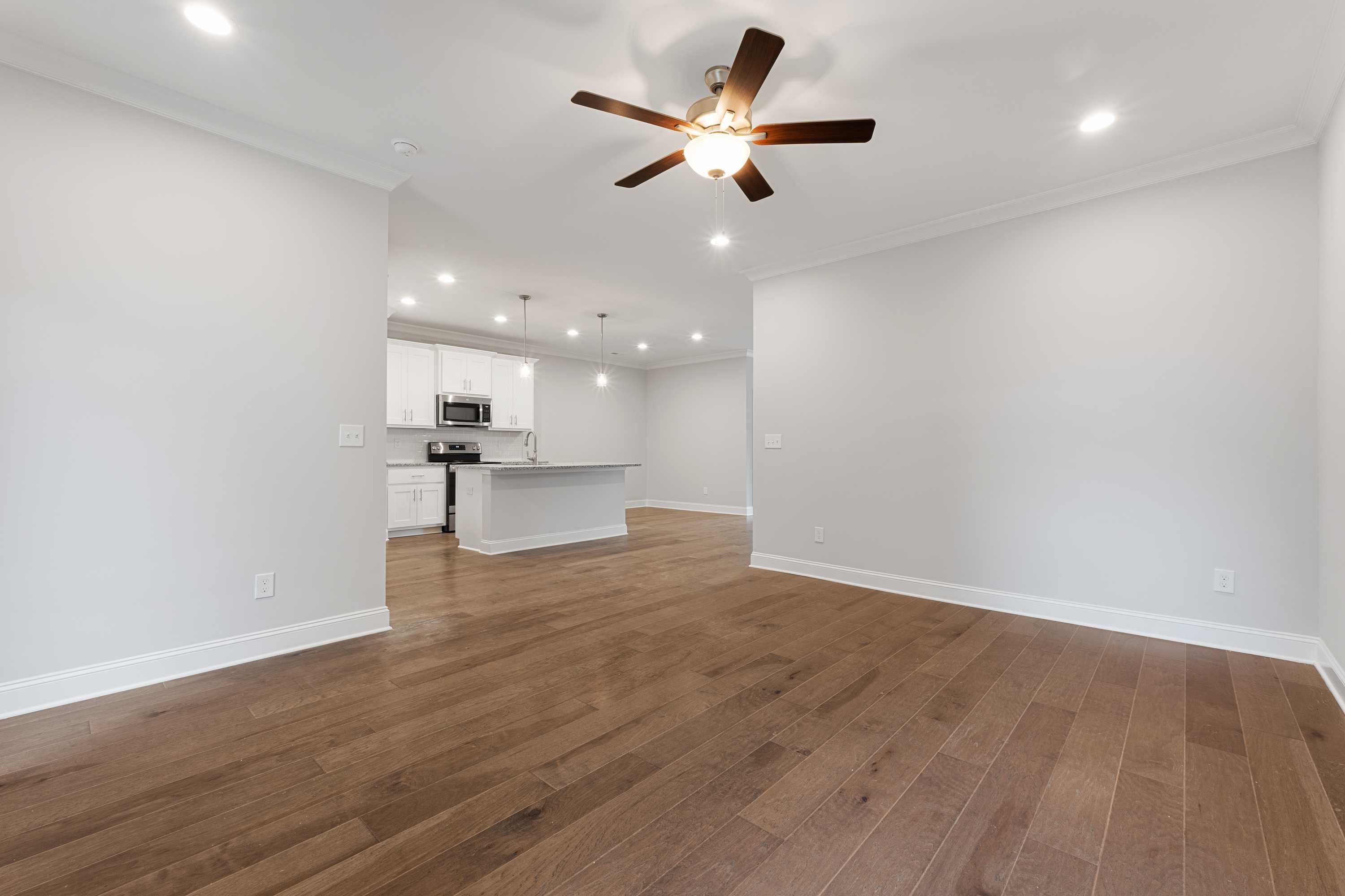 Spacious open-concept living and kitchen in The Copeland B with hardwood floors, white cabinets, island, and ceiling fan