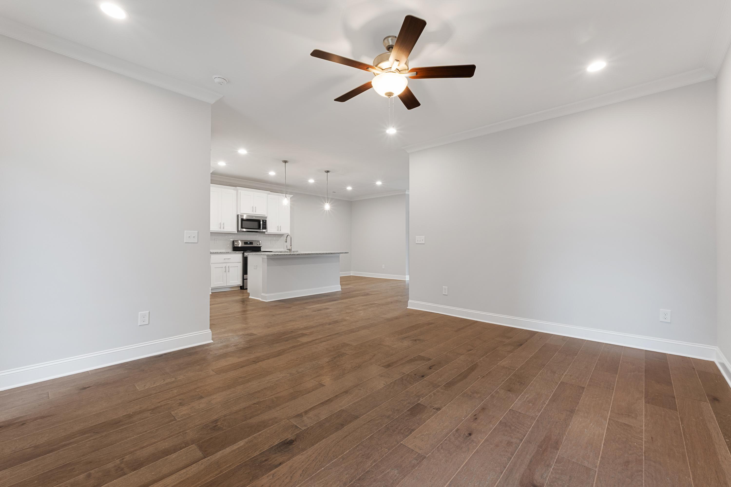 Spacious open-concept kitchen and living area in The Copeland C with hardwood floors, white cabinets, and ceiling fan