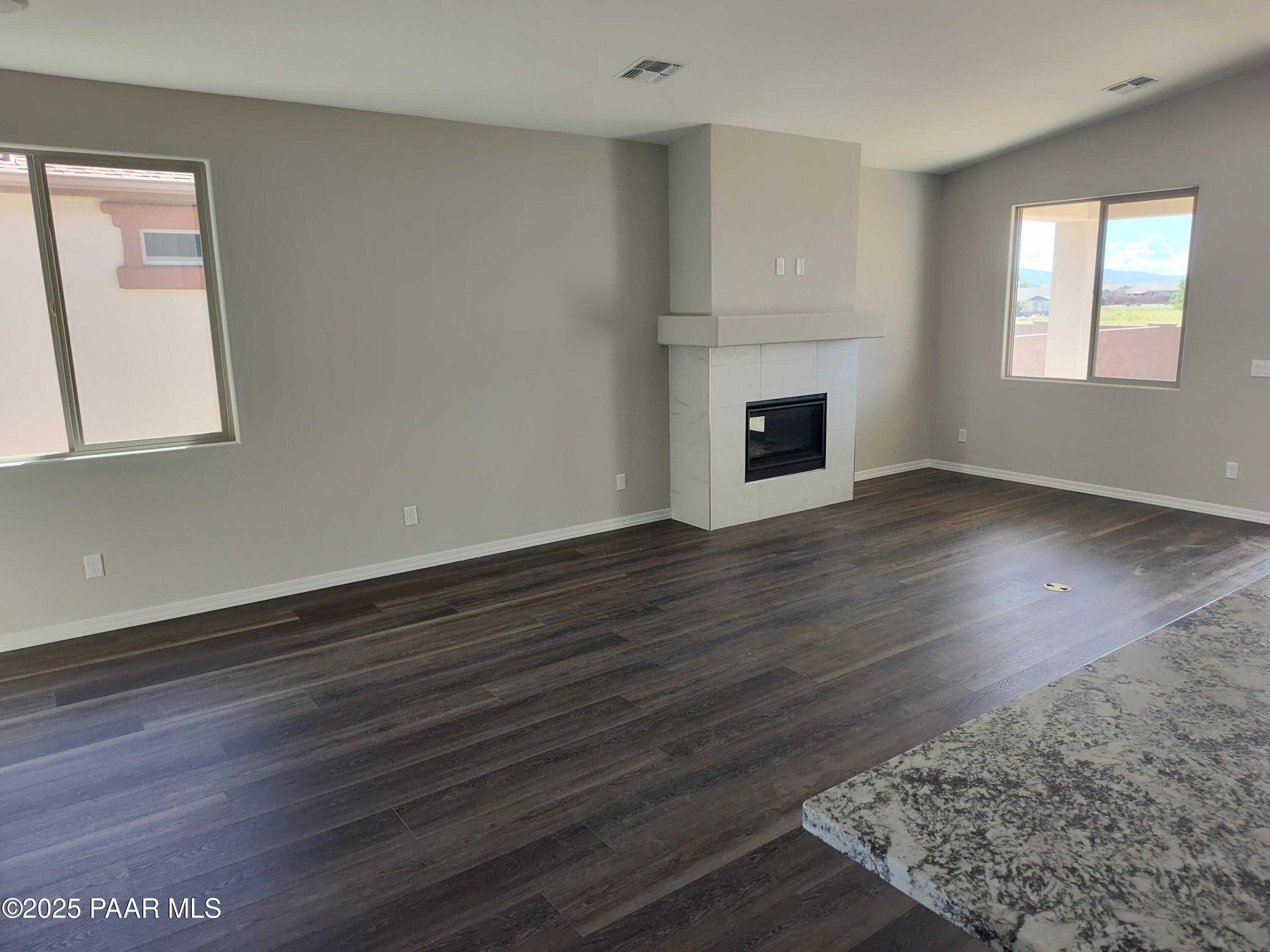 Spacious living room with white stone fireplace, large windows, and wood-look flooring in Davidson Homes The Frontier A, Prescott Valley, Arizona