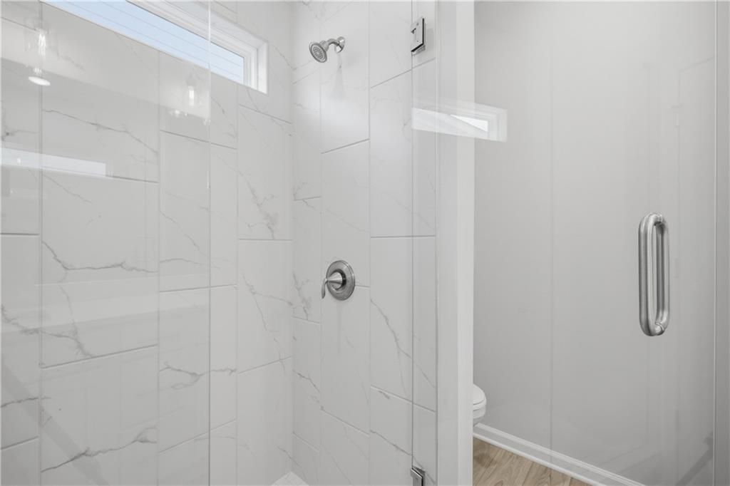 Frameless glass walk-in shower with marble tile and transom window in Davidson Homes The Oconee B, The Bluffs, Canton, Georgia