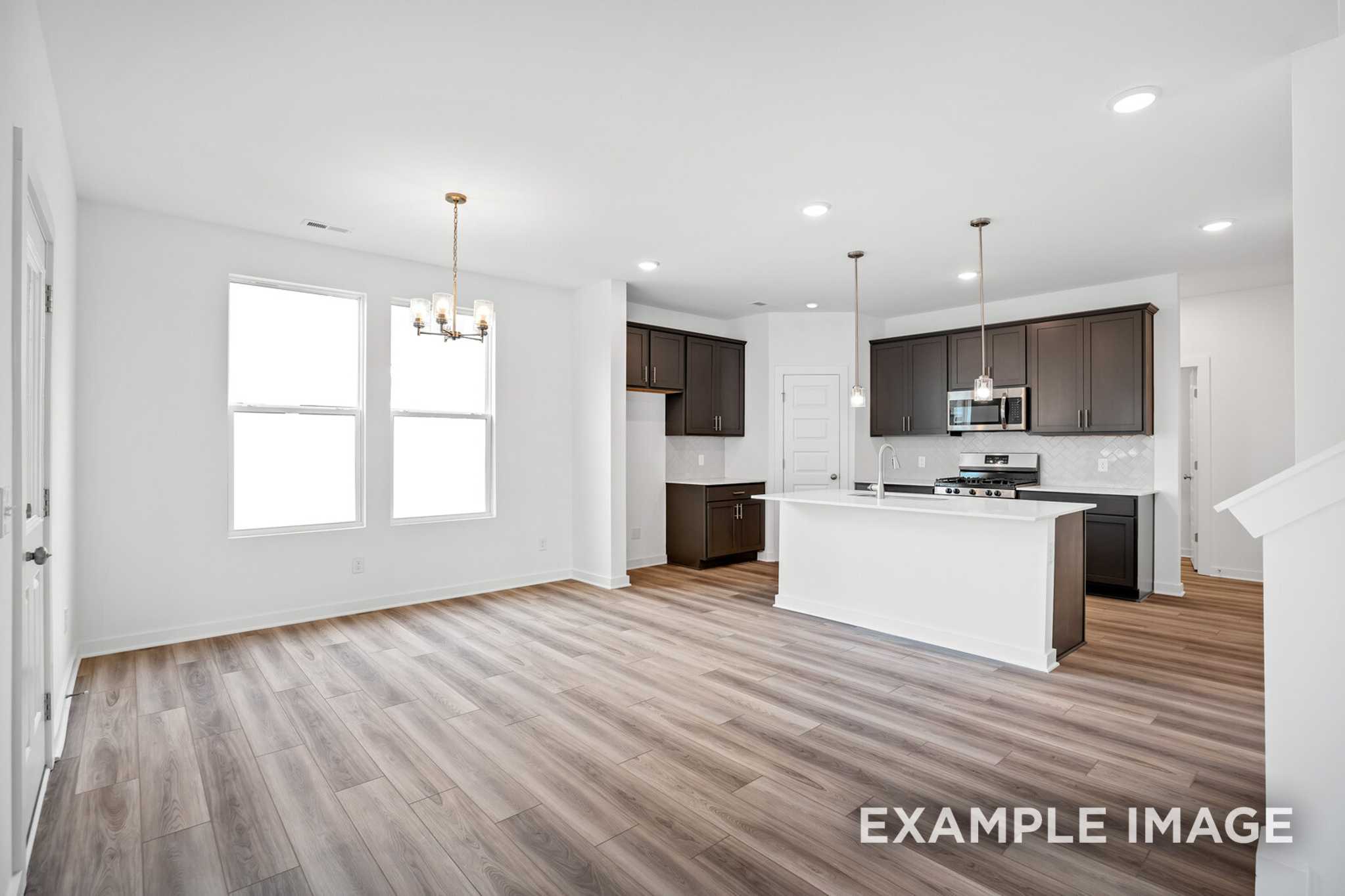 Spacious open-concept kitchen in The Murray B with white island, dark cabinets, large windows, and hardwood floors