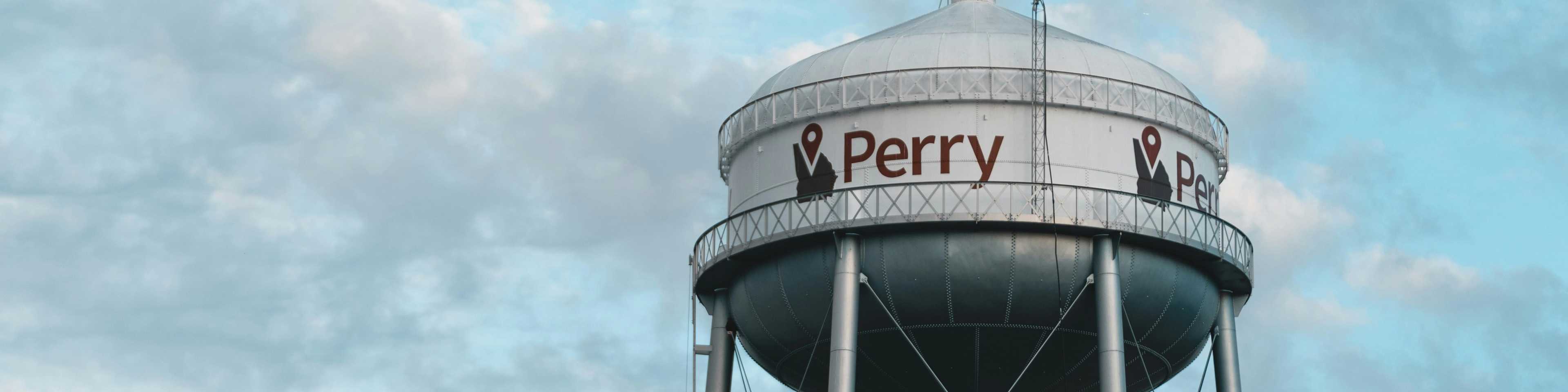 Silver Perry water tower with red city logo under partly cloudy blue skies