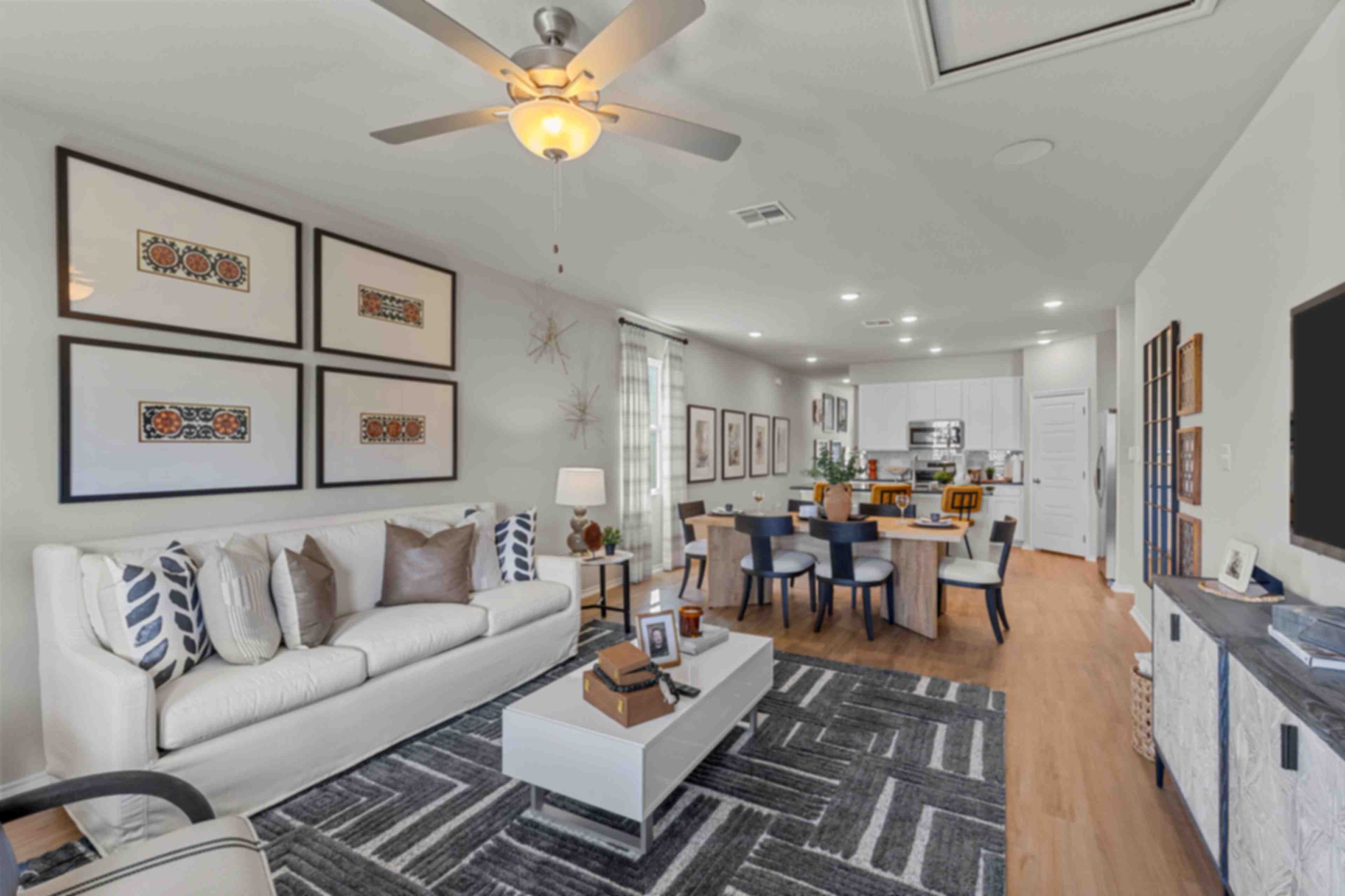 Spacious open-concept living room at Applewhite Meadows San Antonio TX with white sofa, dining table, hardwood floors, and modern wall art