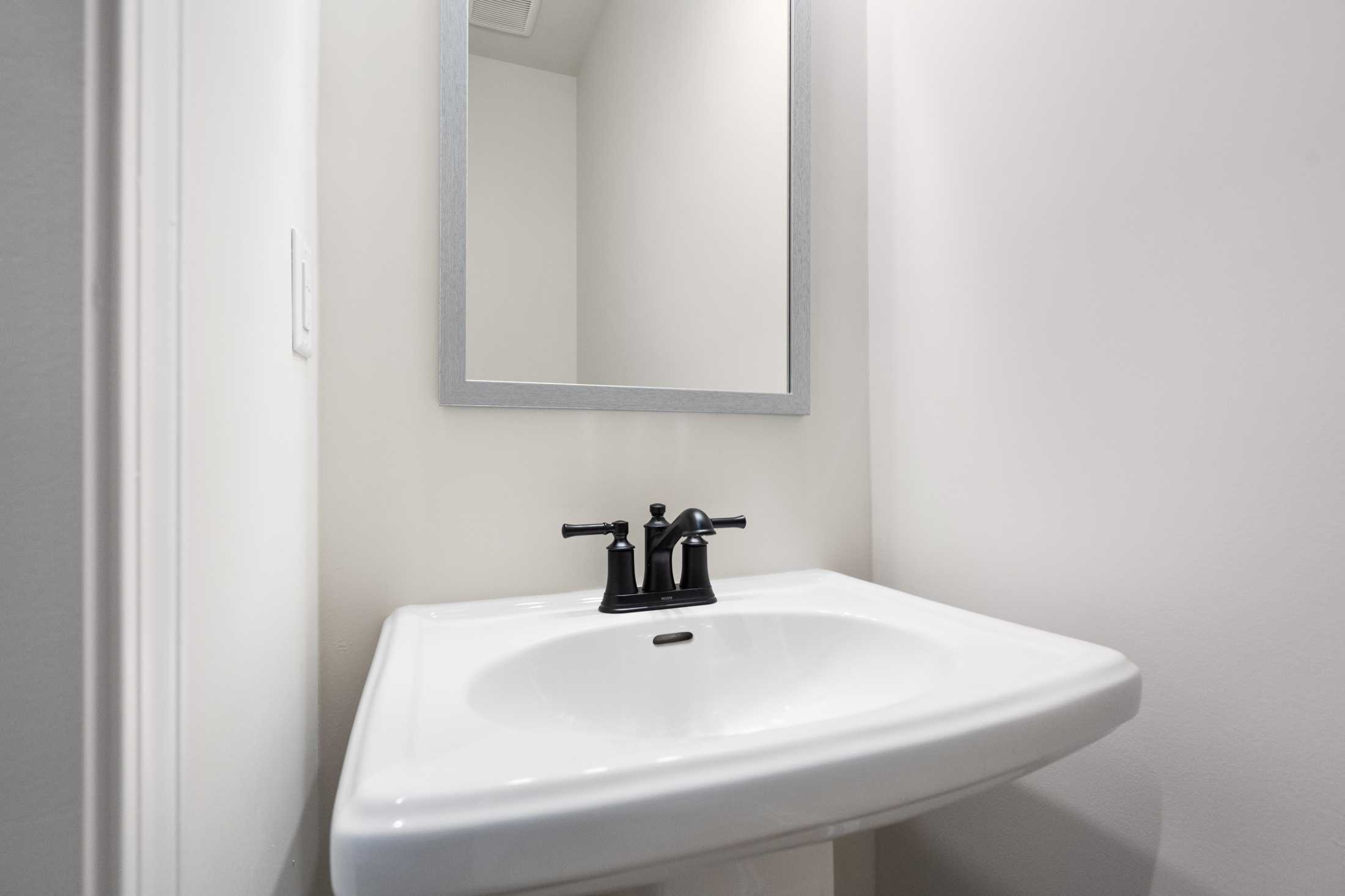Modern powder room in The Cary B home, Kennesaw, with white pedestal sink, black faucet, and large frameless mirror