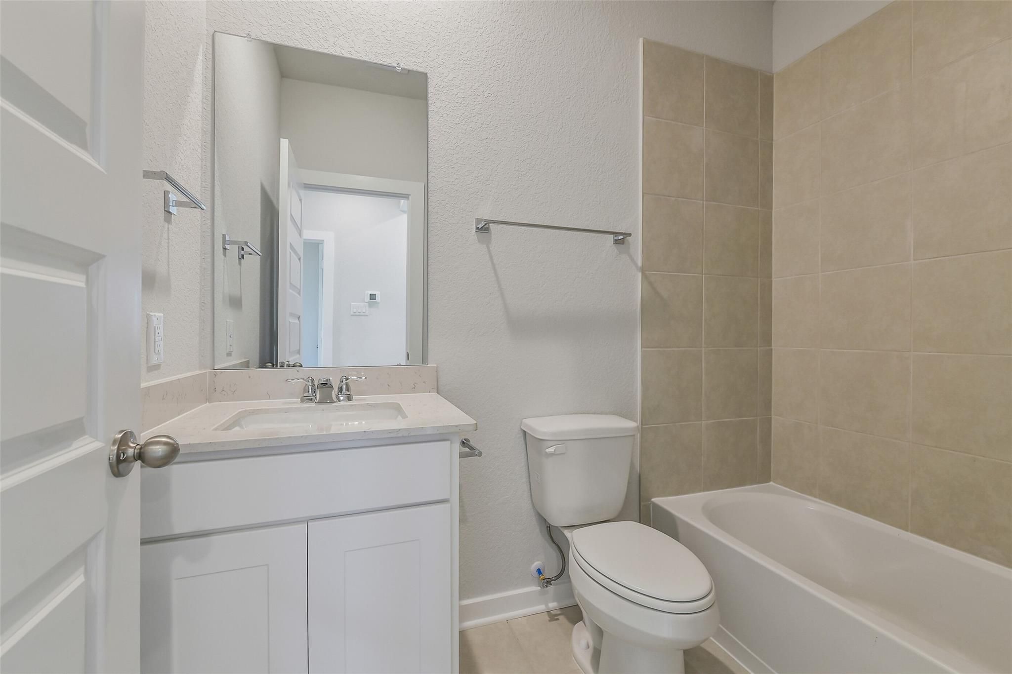 Modern bathroom with white vanity, large mirror, bathtub, and beige tile in Davidson Homes The Frio G, Cleveland, Texas