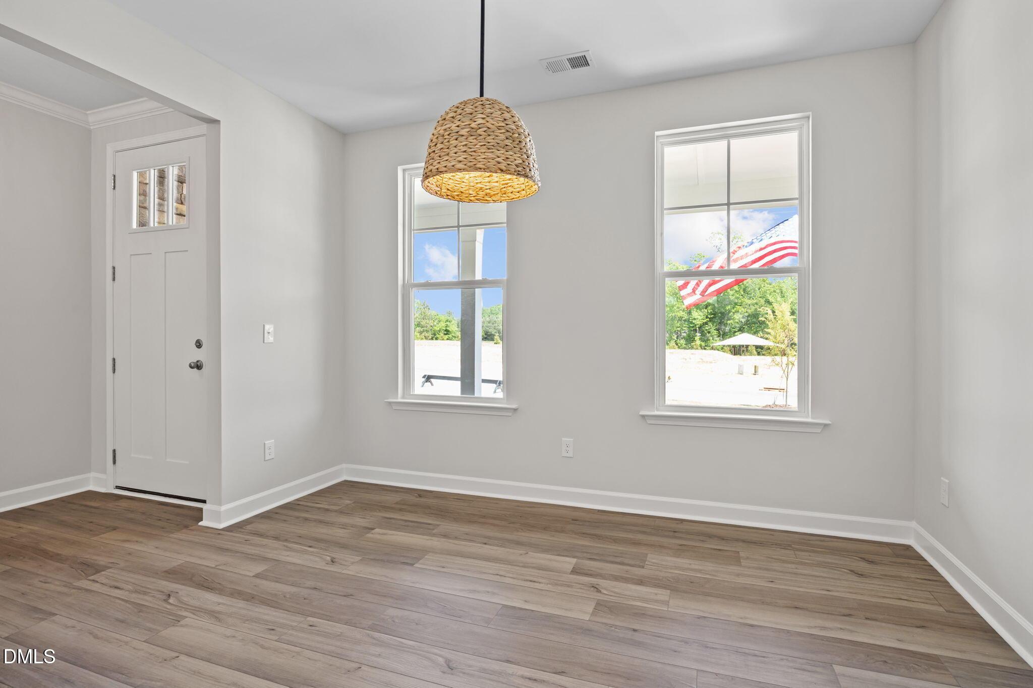 Bright bedroom with hardwood floors, rattan pendant light, and windows overlooking trees and American flag in Davidson Homes The Willow D, Wendell, NC