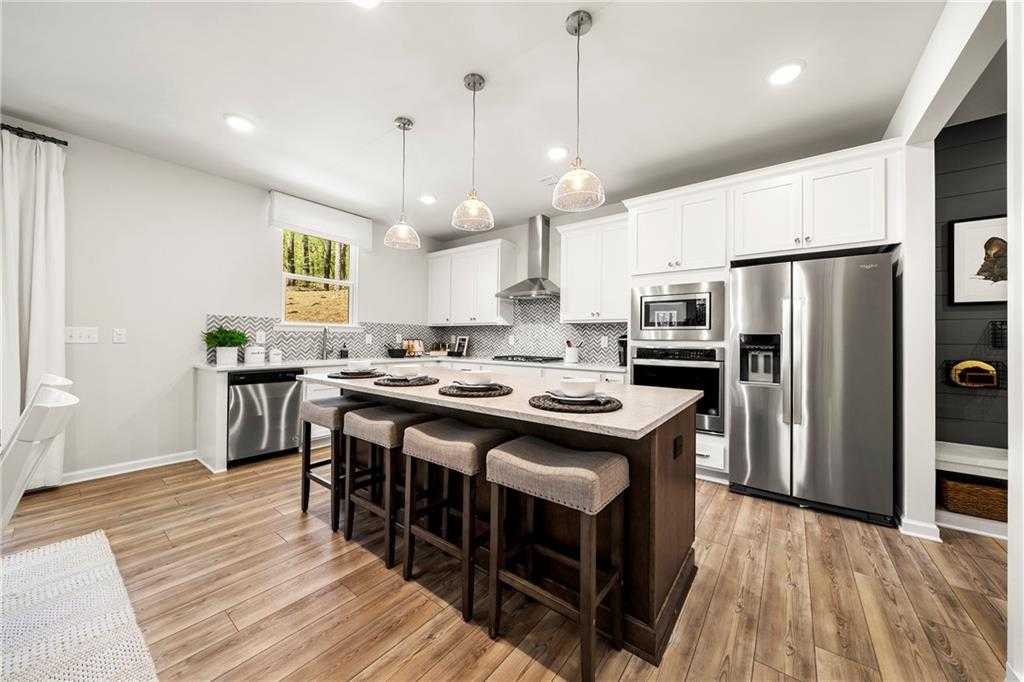 Modern kitchen with white shaker cabinets, stainless steel appliances, pendant lights, and wood island bar in Davidson Homes The Hickory B, Riverwood, GA