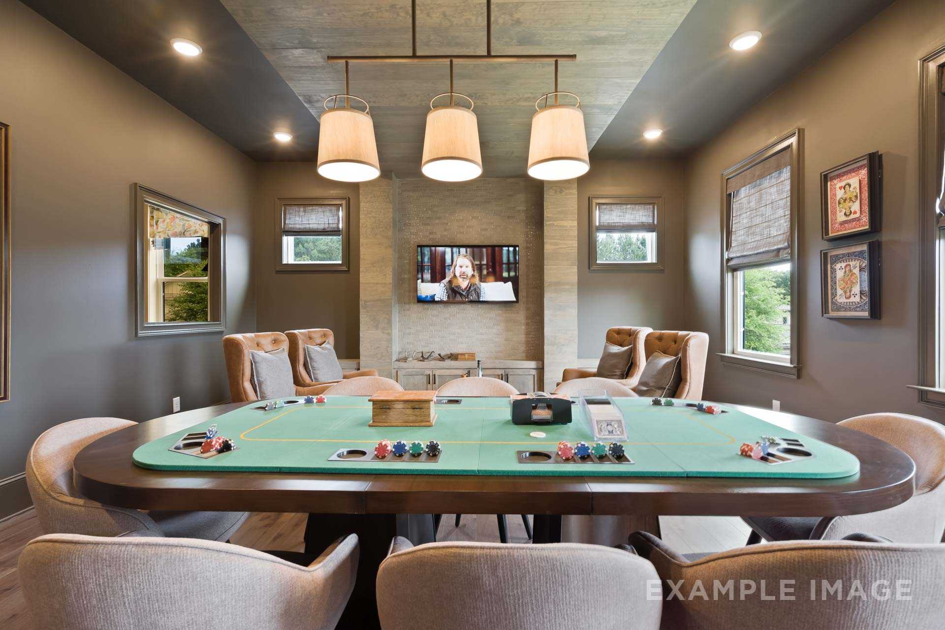 Spacious game room in The Seaside home design featuring green felt poker table, mounted TV, and tufted armchairs