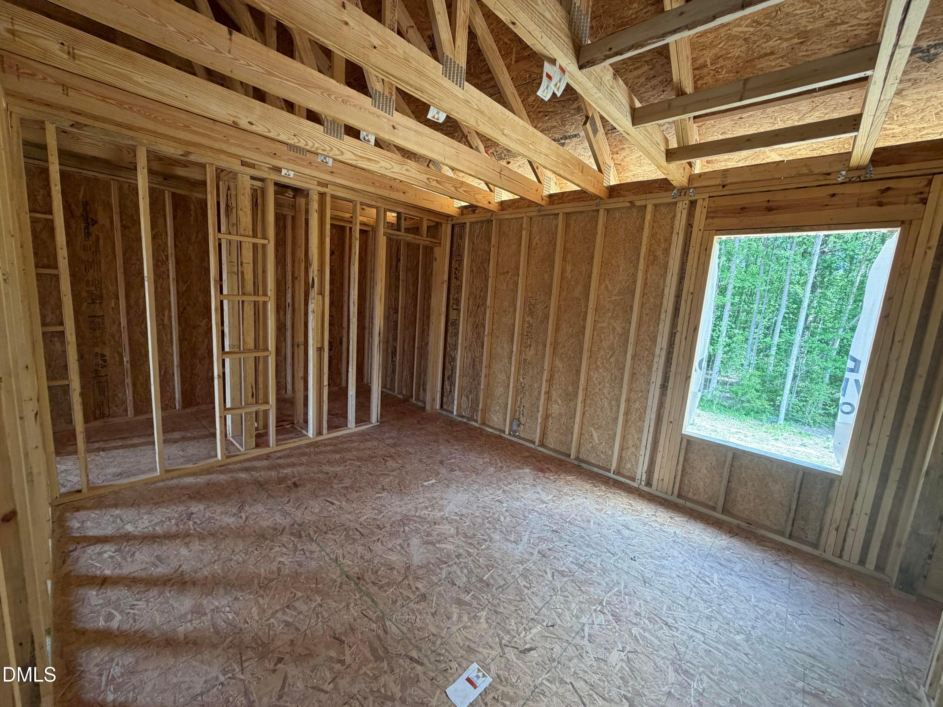 Exposed wooden framing, trusses, and plywood subfloor in spacious room with large window overlooking trees in Davidson Homes The Hickory II C, Lillington, NC