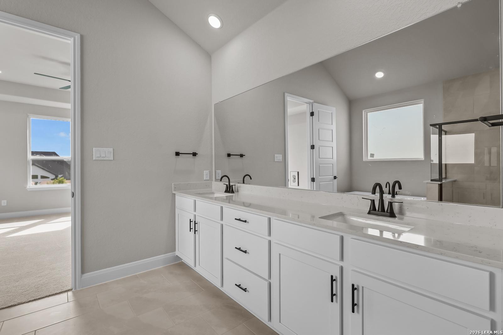 Double vanity bathroom with white cabinets, quartz countertops, and matte black faucets in Davidson Homes Foster E plan, Castroville TX