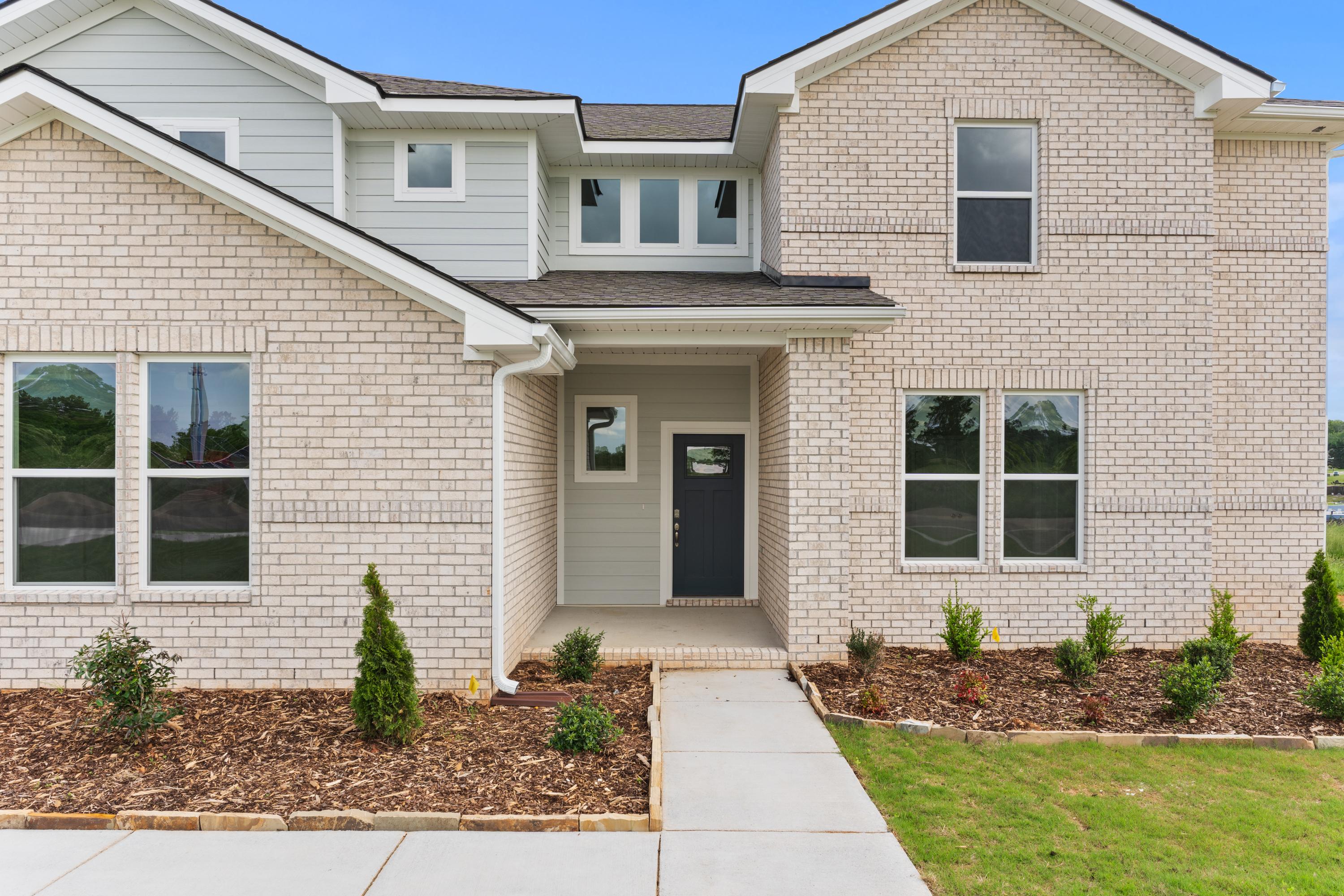 Modern beige brick exterior of The Haven E 1-story home with covered entry, large windows, and landscaped yard in Owens Cross Roads