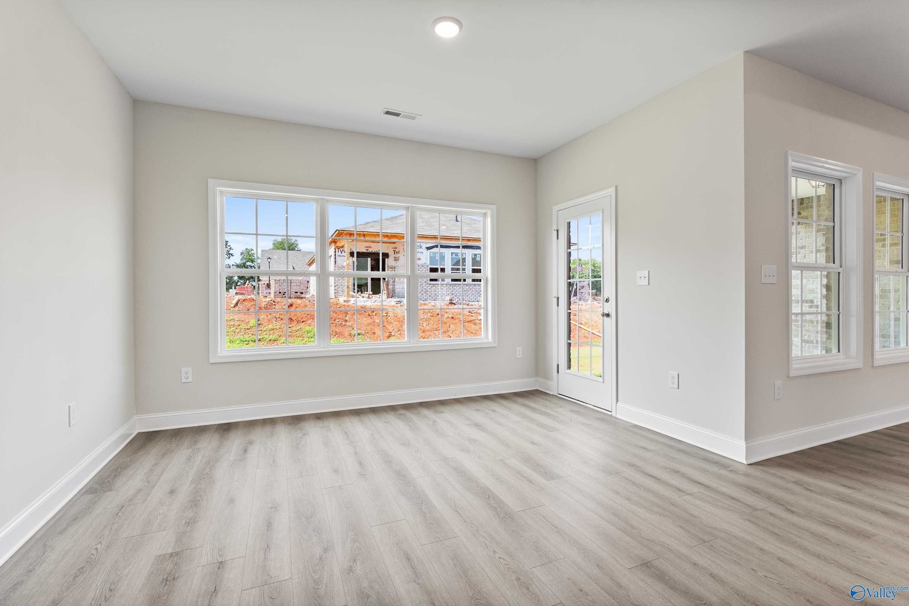 Bright living room with large windows overlooking new home construction, beige walls, and hardwood floors in The Finleigh, Toney, Alabama