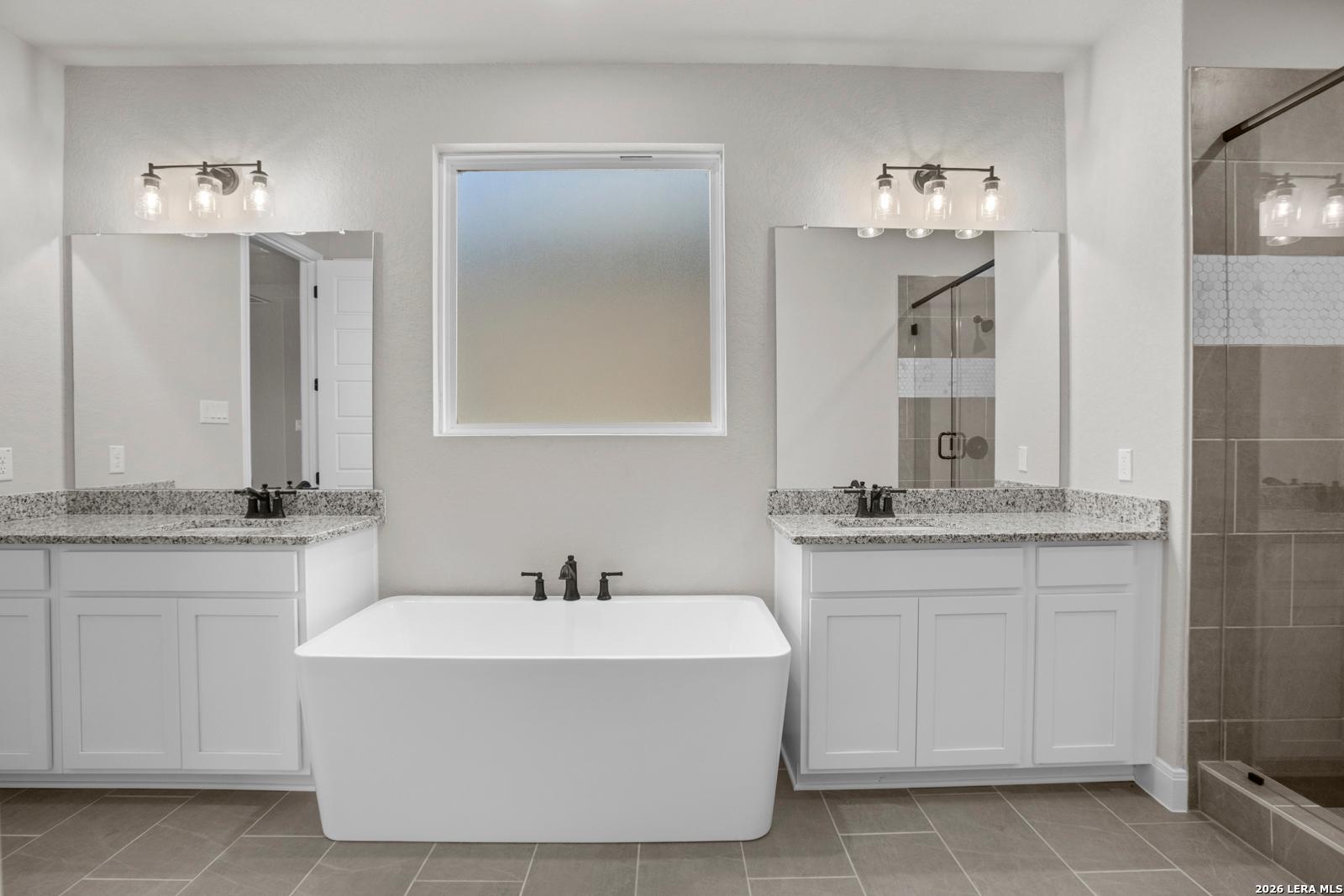 Modern primary bathroom with dual vanities, soaking tub, and tile shower in Davidson Homes The Jennings G, Ladera, San Antonio