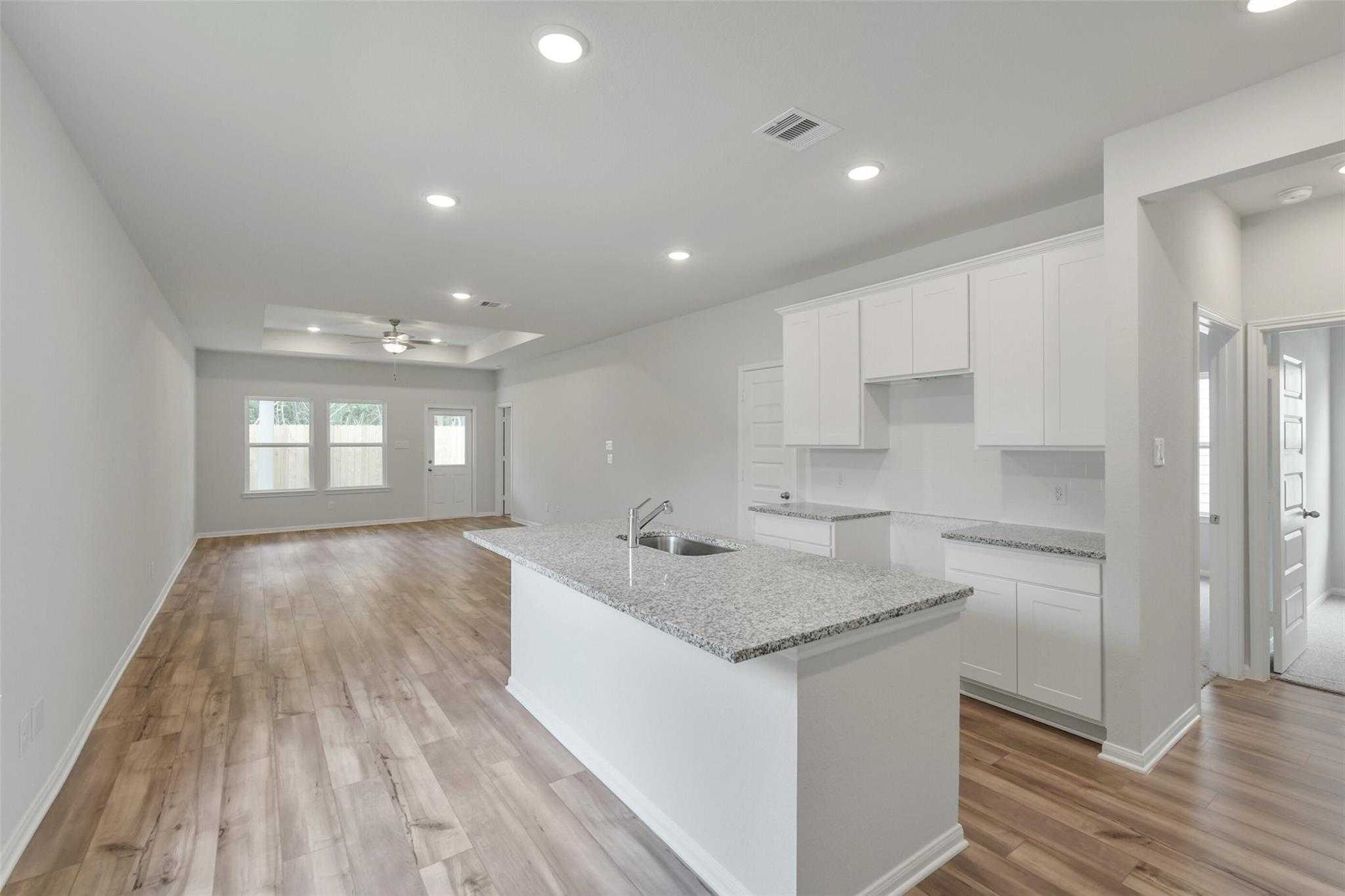 Modern open kitchen with white cabinets, granite island sink, and wood floors in Davidson Homes The Frio G, Conroe, Texas