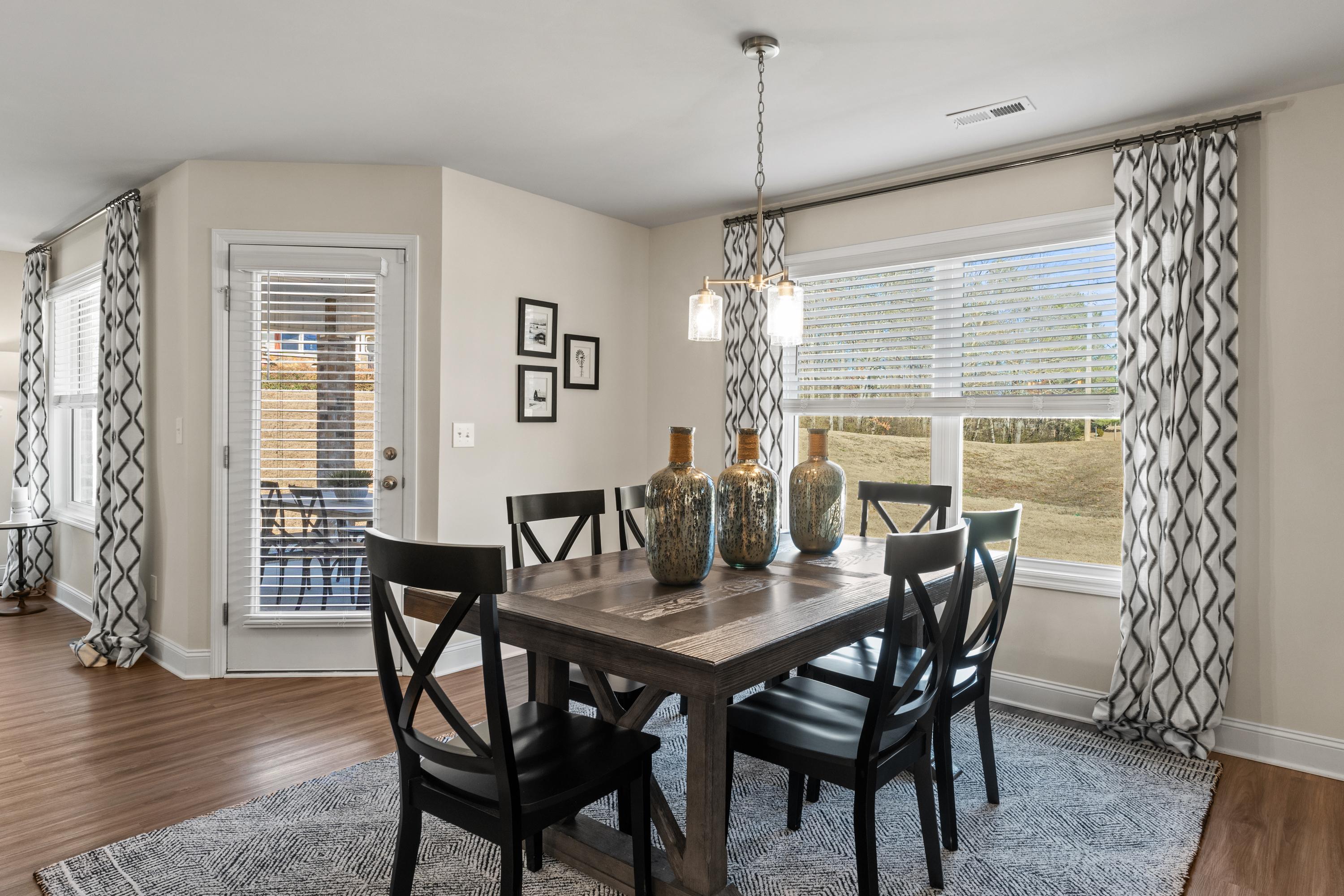 Spacious dining room in Berry Cove home with wooden farmhouse table, black chairs, pendant lights, and large windows in New Market Alabama