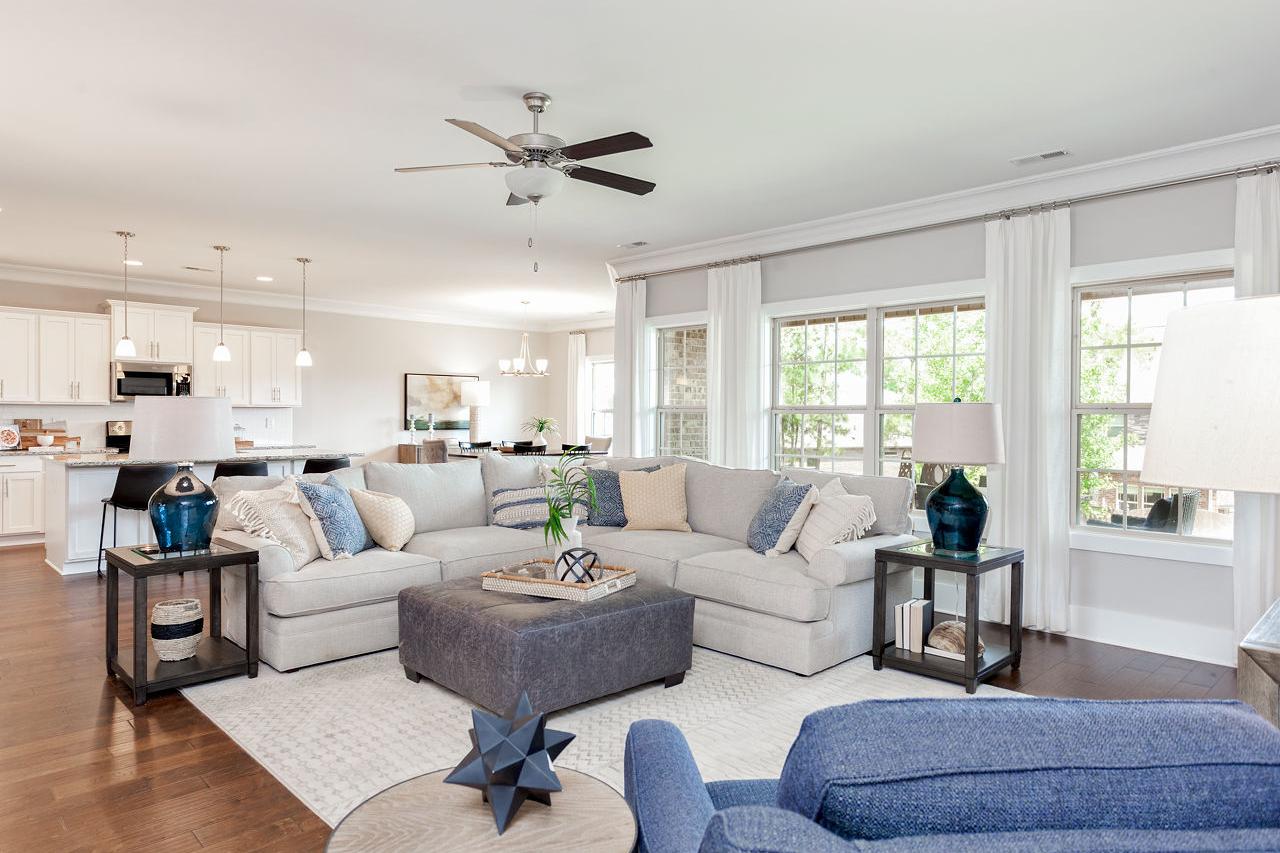 Spacious open-concept living room in The Rockford home with L-shaped gray sofa, ceiling fan, and adjacent white kitchen island