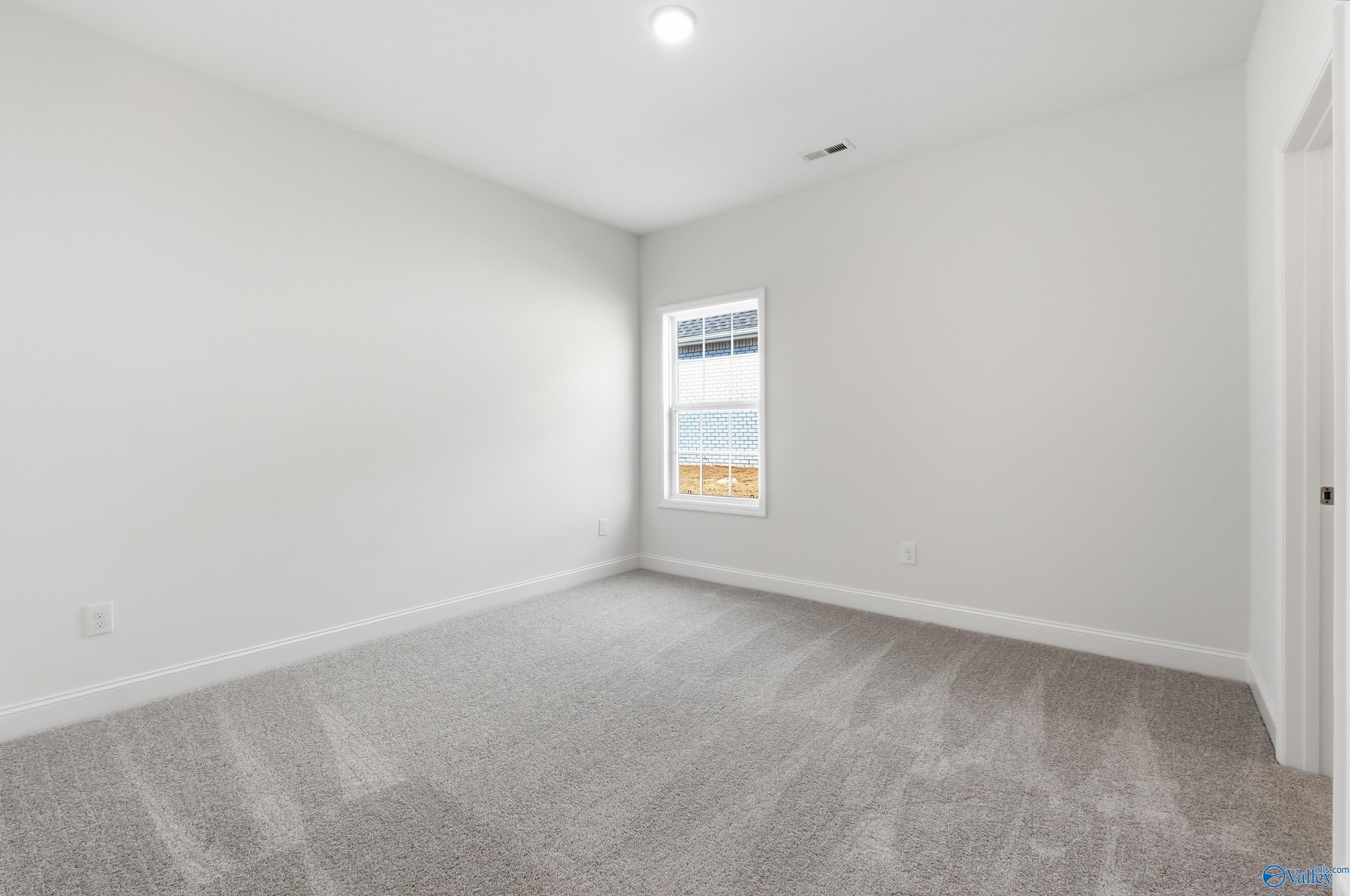Empty secondary bedroom featuring light gray walls, carpet flooring, and large window in Davidson Homes The Montgomery C, Harvest, Alabama