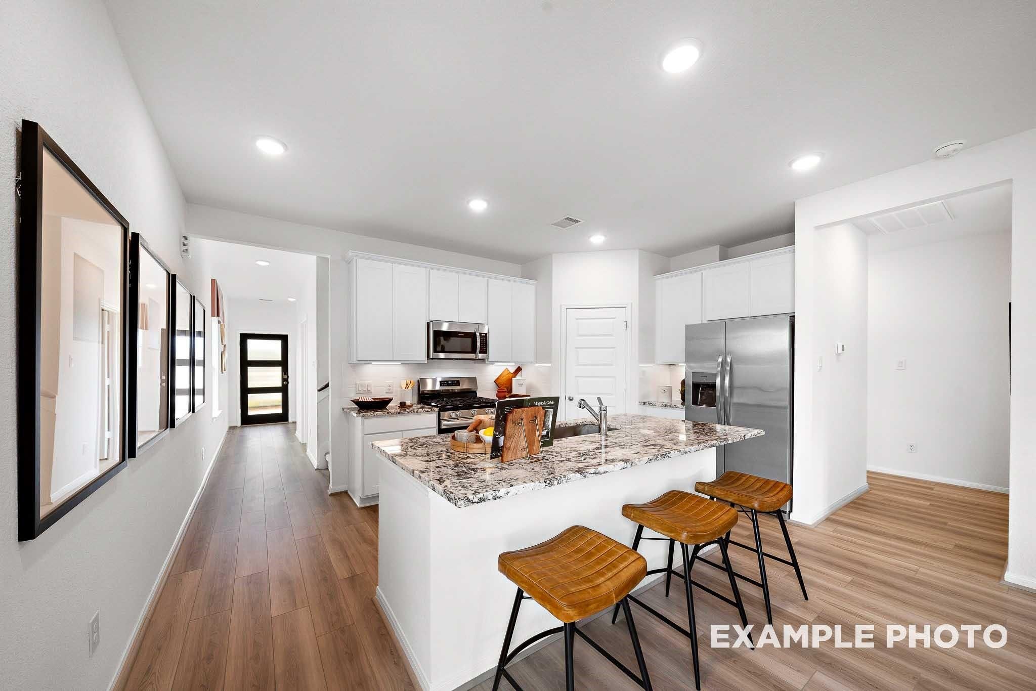 Modern kitchen featuring white shaker cabinets, granite island with wood stools, stainless appliances in Davidson Homes The Sabine F, Magnolia, Texas
