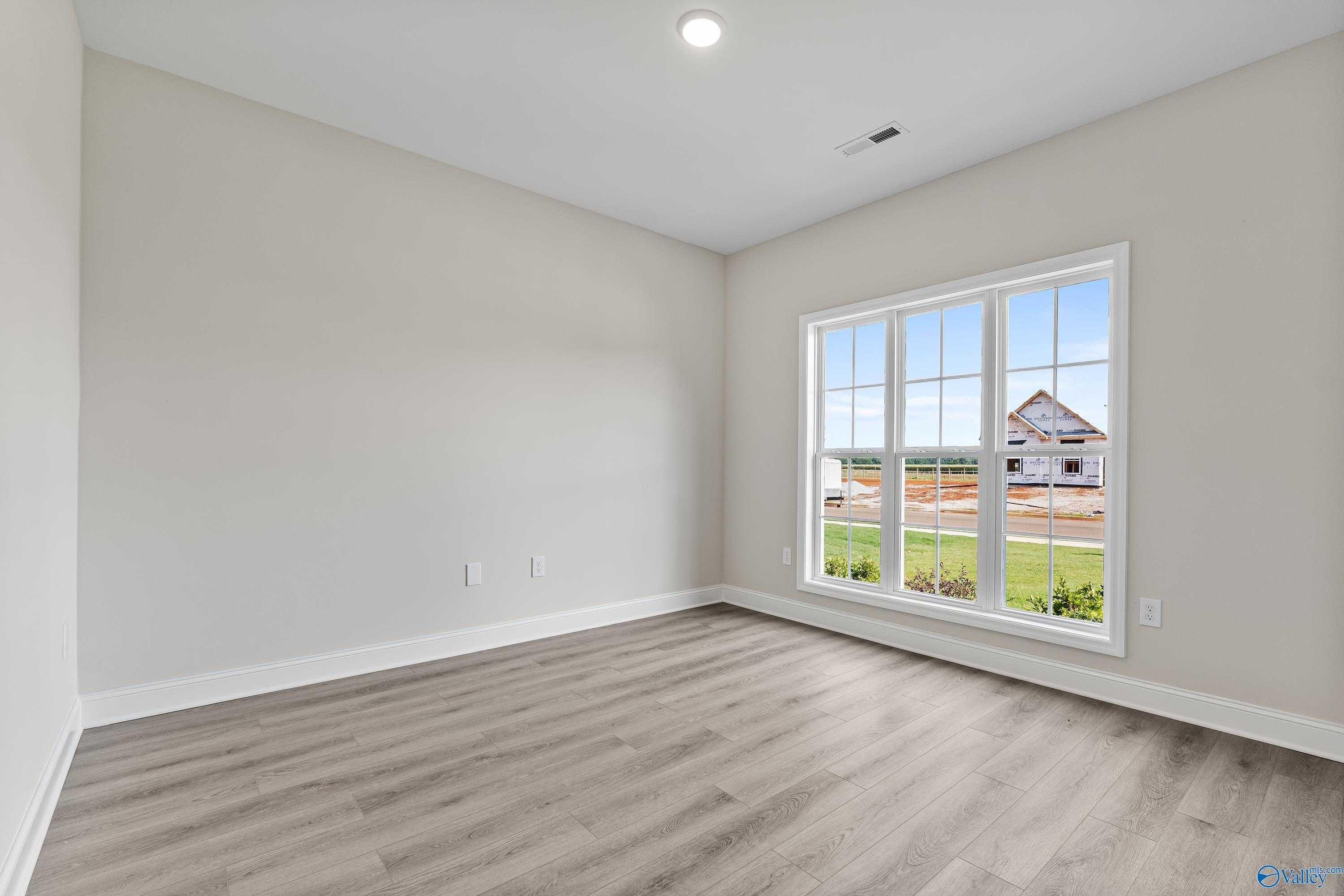 Bright bedroom with neutral walls, luxury vinyl plank floors, and large window view of green backyard in The Finleigh, Toney, Alabama